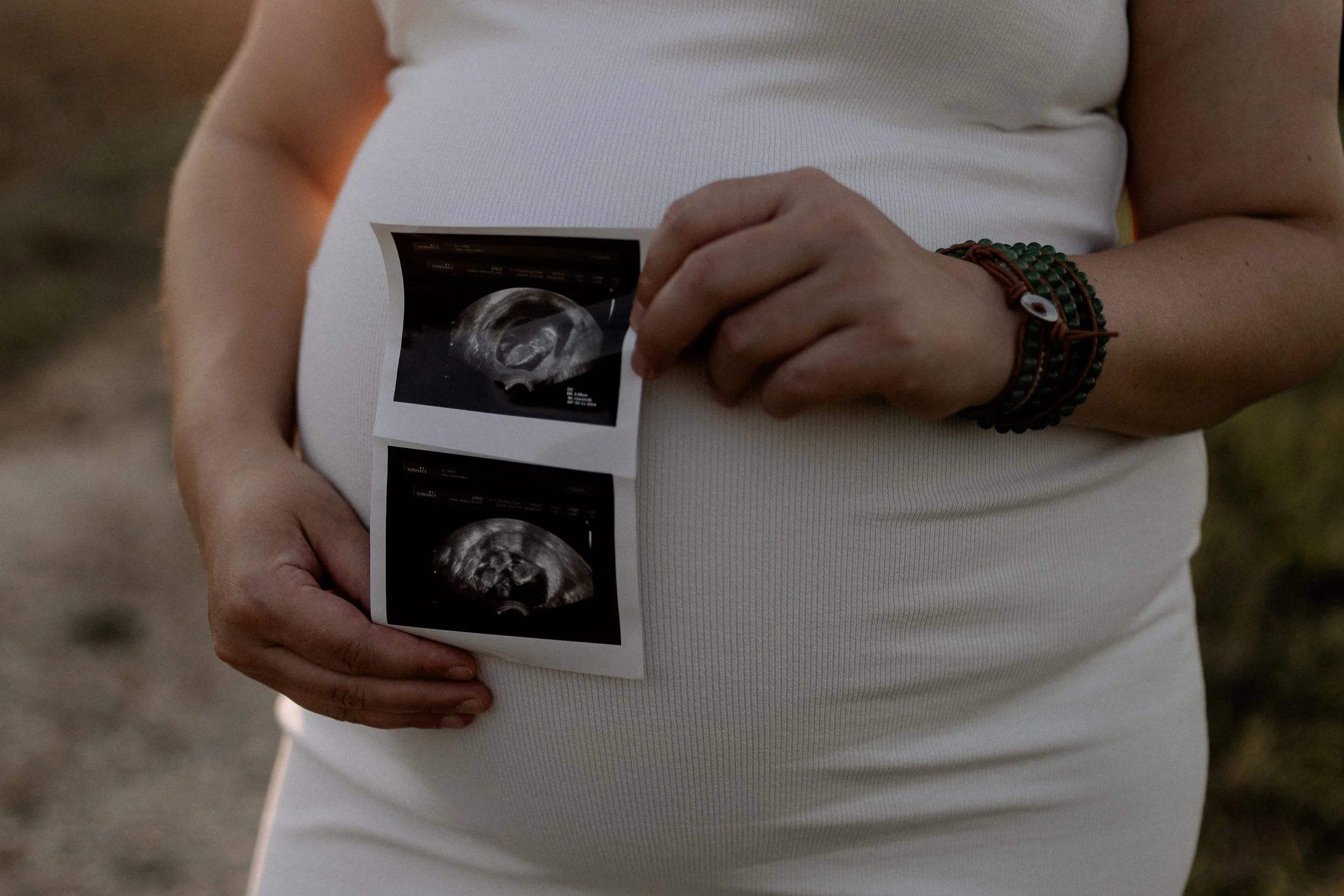 Eine schwangere Person hält Ultraschallbilder ihres ungeborenen Kindes in der Hand, während sie draußen steht.