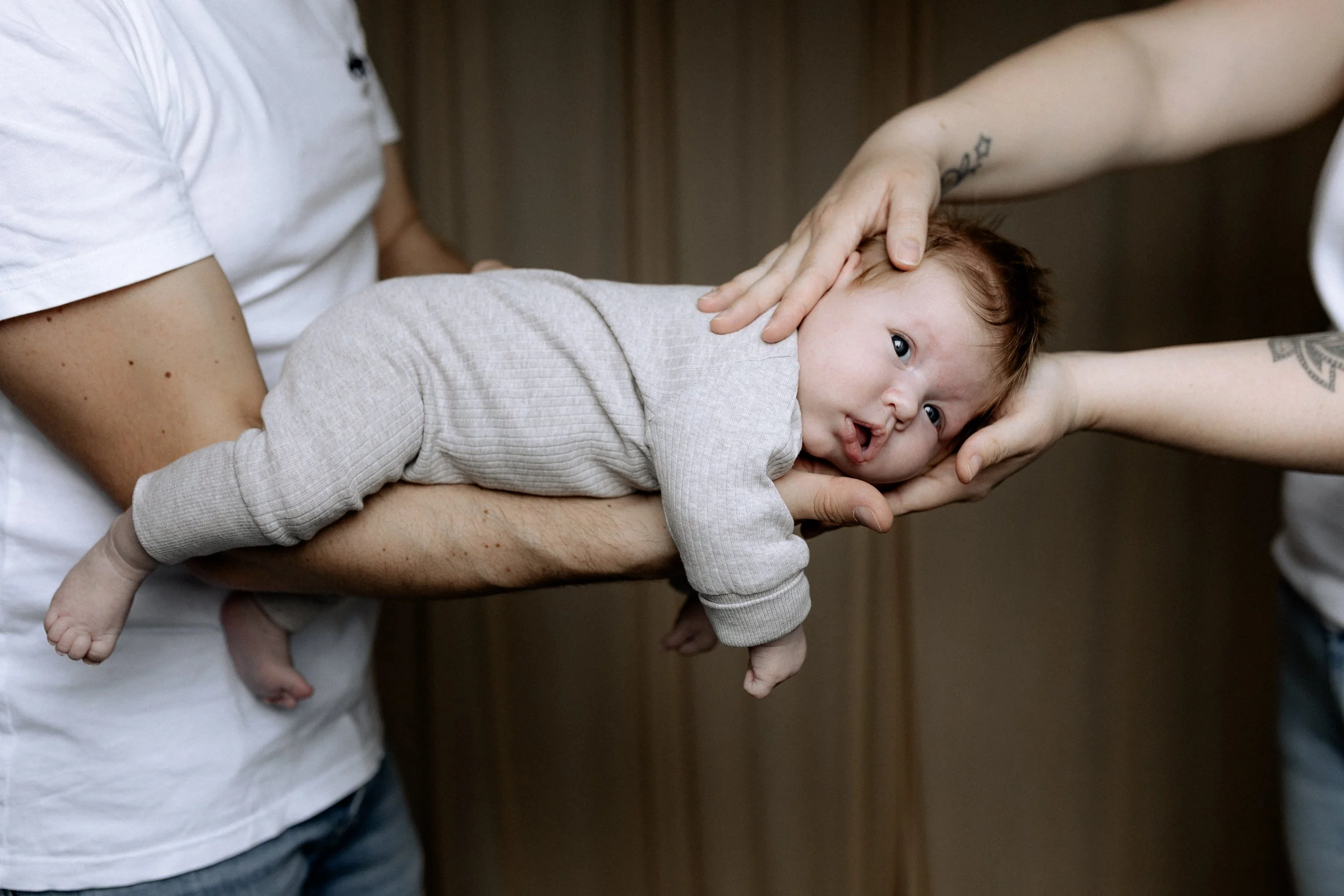 Ein Baby liegt auf einer Erwachsenenarmstütze, während zwei Personen es sanft hält und es auf seinem Gesicht berührt.