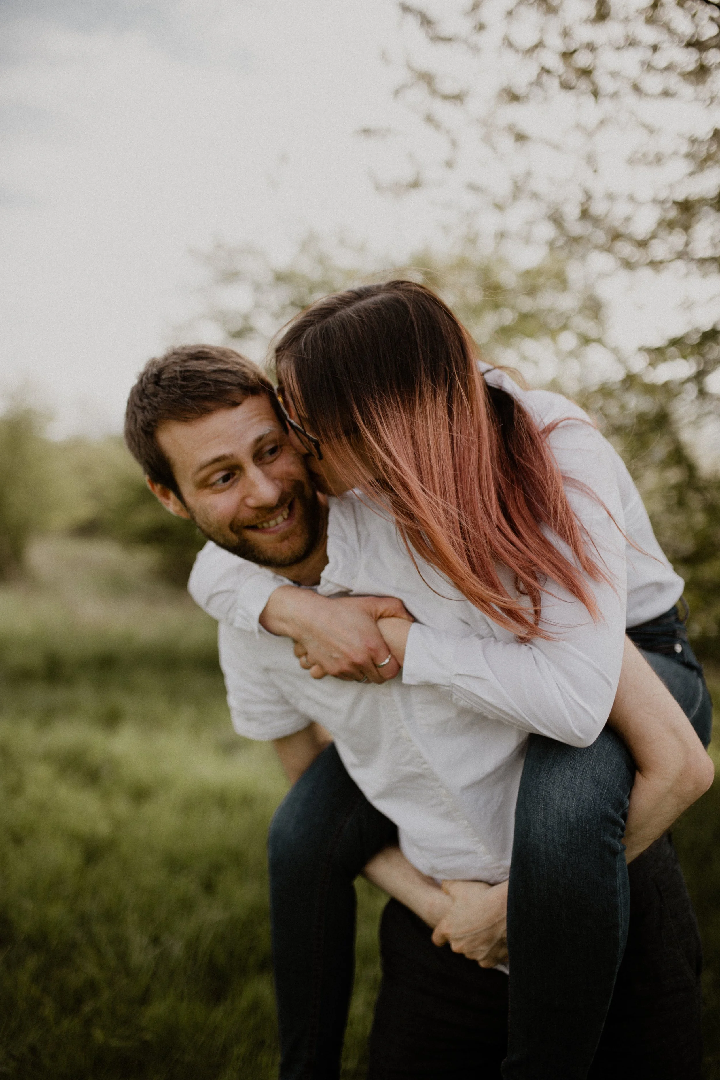 Ein glückliches Paar beim Spaß im Freien, sie ist auf seinem Rücken, es ist ein lauer Tag mit Bäumen im Hintergrund.