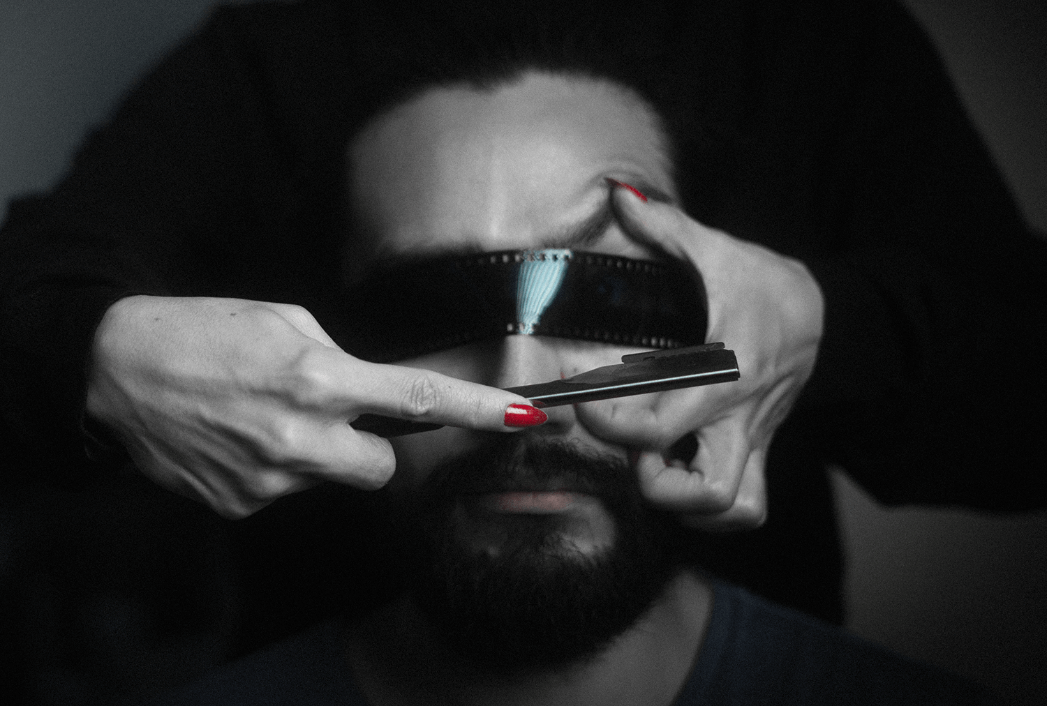 Black and white image of a man with dark hair and beard wearing dark sunglasses, holding a razor blade under his nose, with his index finger and thumb pinching the blade.