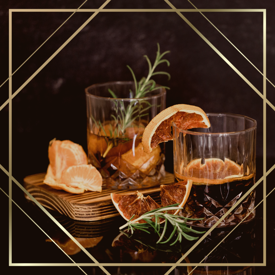 Two glasses of dark liquor garnished with citrus slices and rosemary with citrus peels and rosemary sprigs around on a wooden board against a dark background.