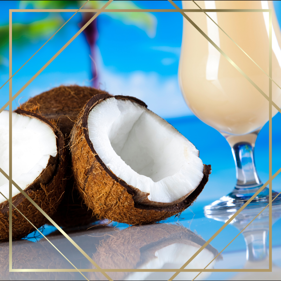 Halved coconut with white flesh and a glass of coconut milk on a blue surface.