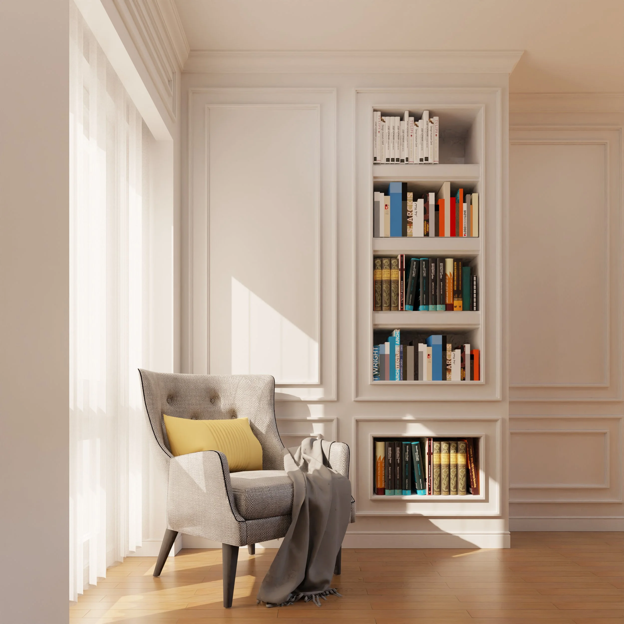 A cozy reading nook with a gray armchair with a yellow pillow, a blanket, and a bookshelf filled with books. The room has white walls, crown molding, and hardwood flooring.