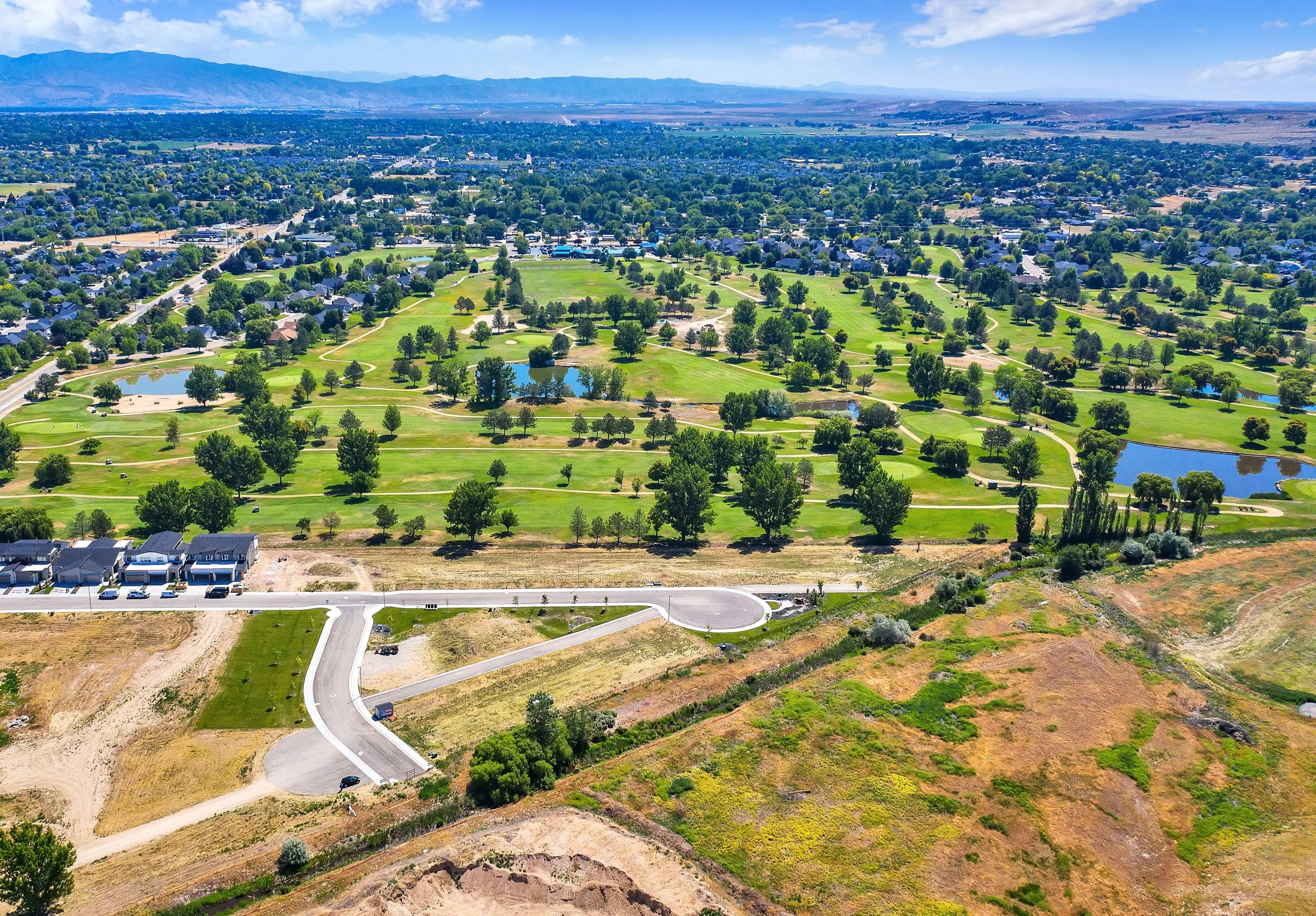 Aerial view of a suburban golf course with lakes and trees, surrounded by residential neighborhoods and a hilly landscape in the background.