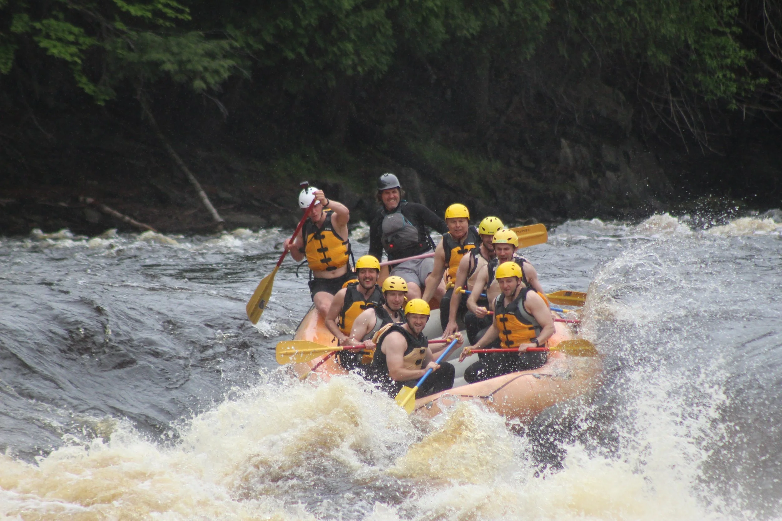 Group of people white water rafting on river, wearing helmets and life jackets, paddling together.