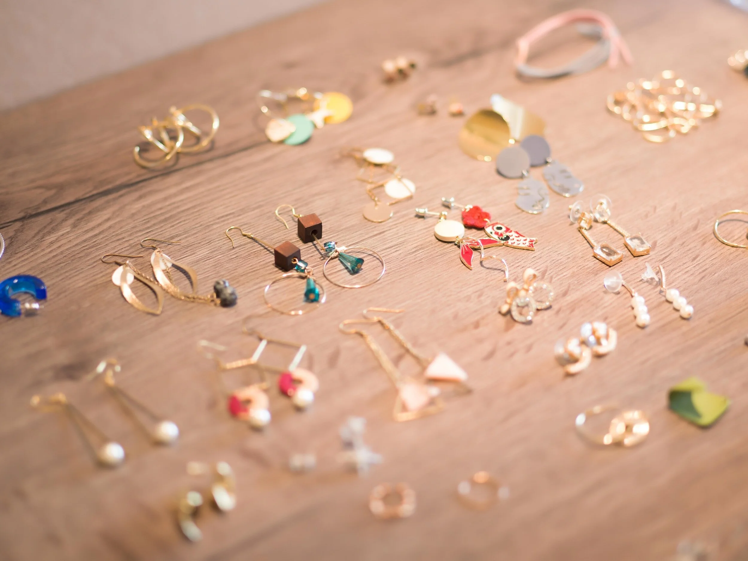 Assorted earrings and jewelry scattered on a wooden surface, including hoops, dangles, and stud earrings in various colors and designs.