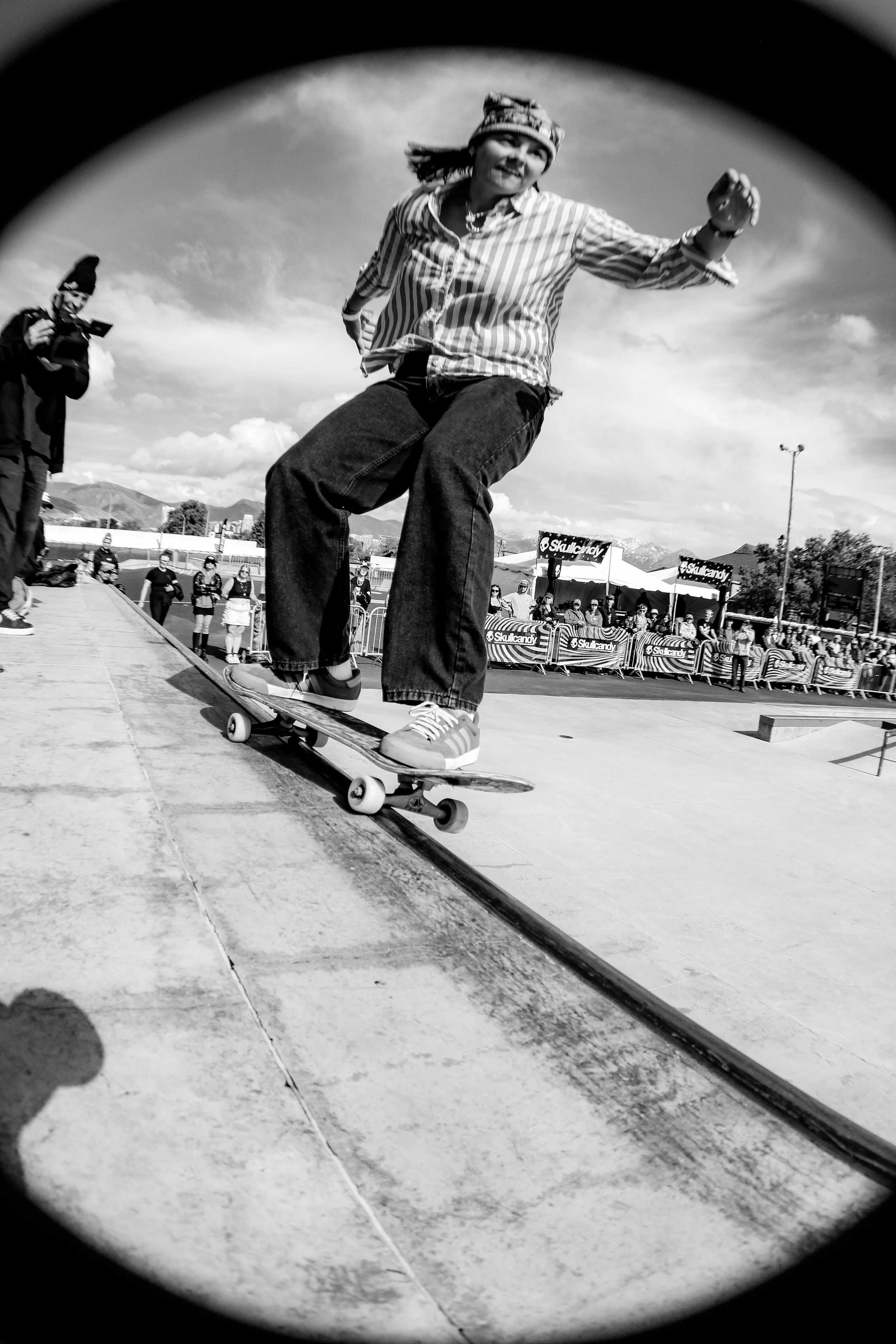 A woman skateboarding at an outdoor skatepark during a sunny day, with spectators watching in the background.