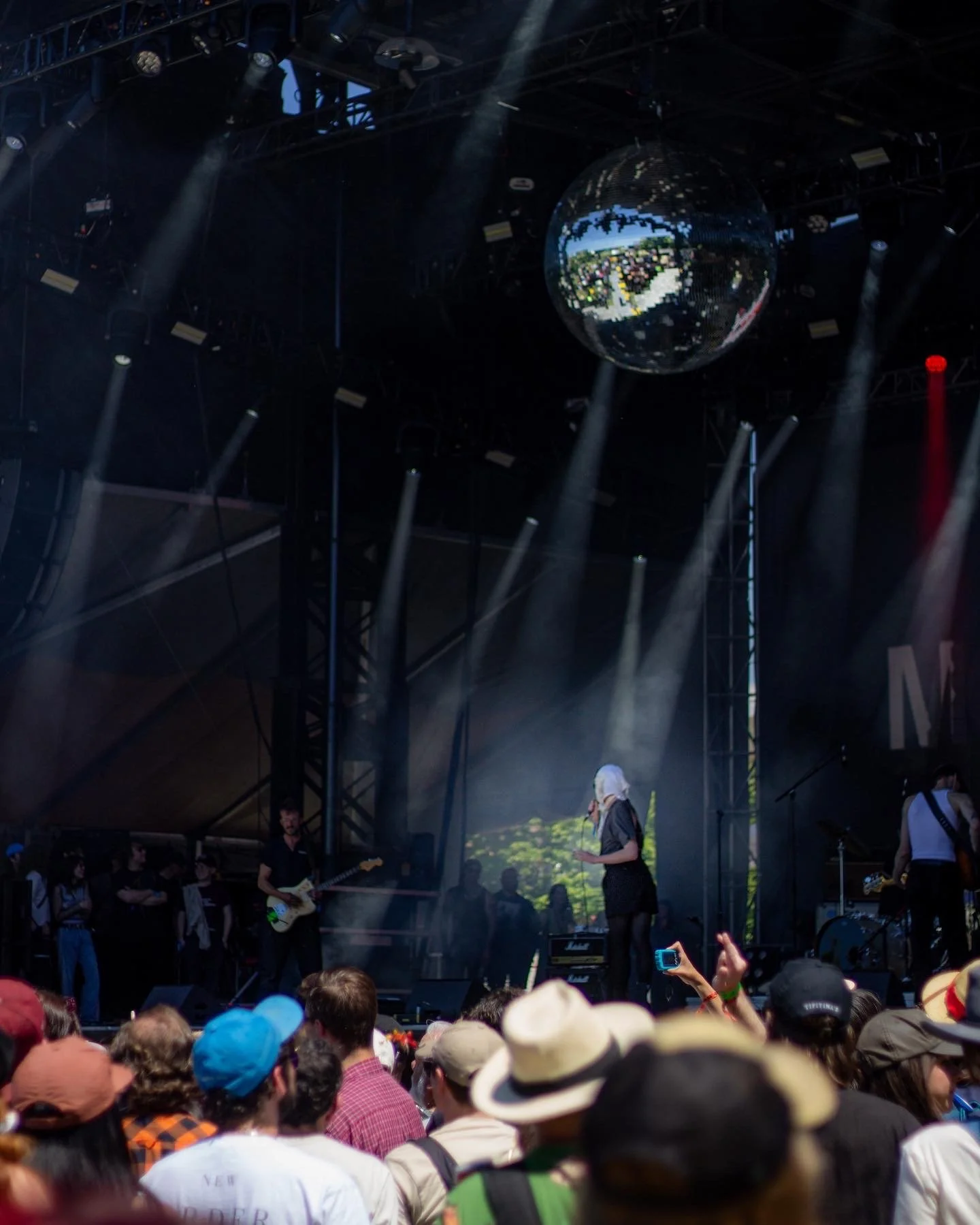 A concert stage with performers and a crowd, featuring a large disco ball hanging from the ceiling and stage lights shining down.