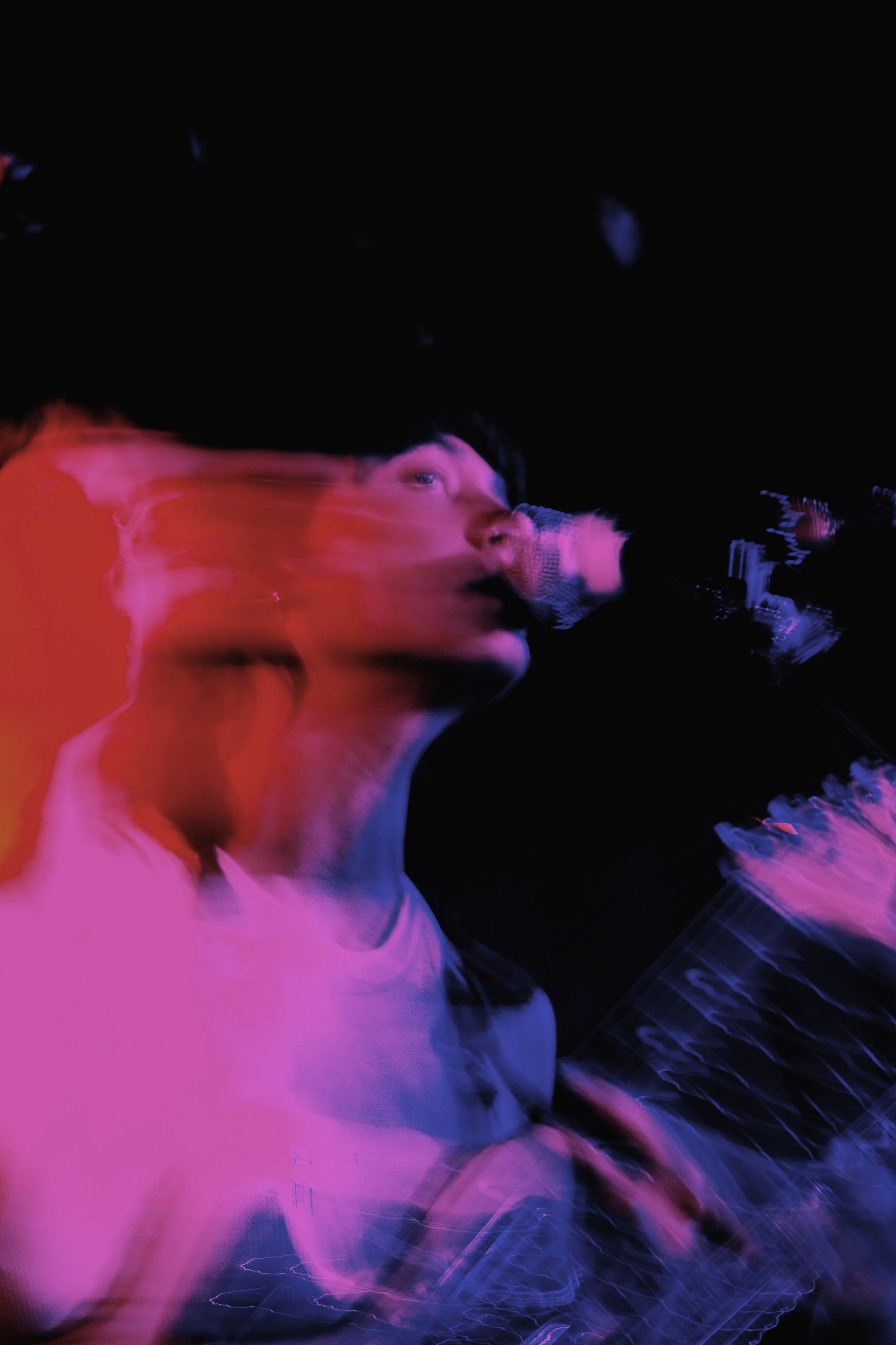 A person performing live music on stage, holding a microphone with colorful lighting effects creating motion blur.