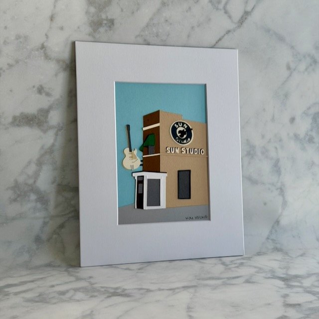 Sun Studio paper illustration shown at an angle, guitar and building layers lifting off the light blue sky