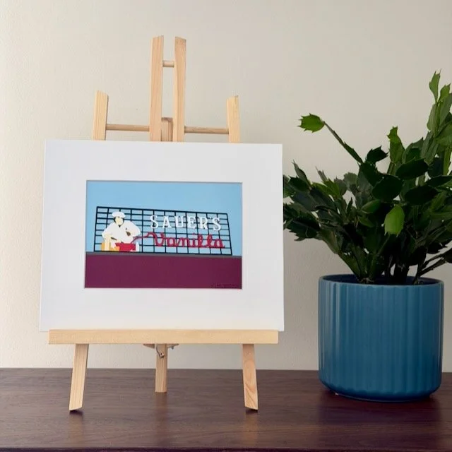 C.F. Sauer's Sign original paper illustration on a small easel on a black metal shelf beside a green plant