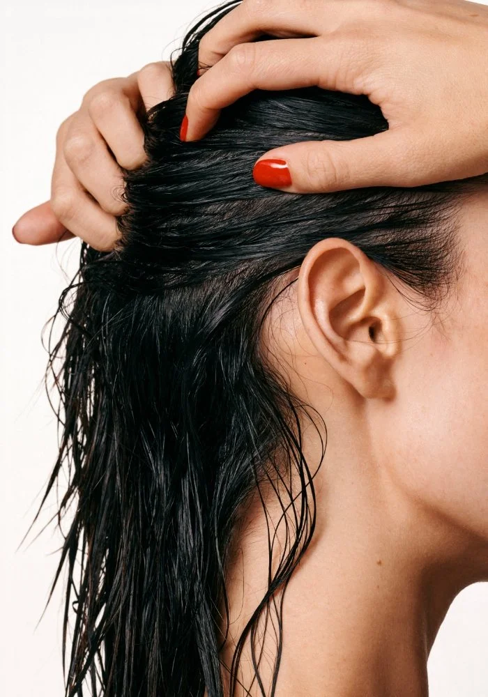 Une personne aux cheveux noirs qui se tient la tête avec une main, montrant l'oreille et le côté du visage.