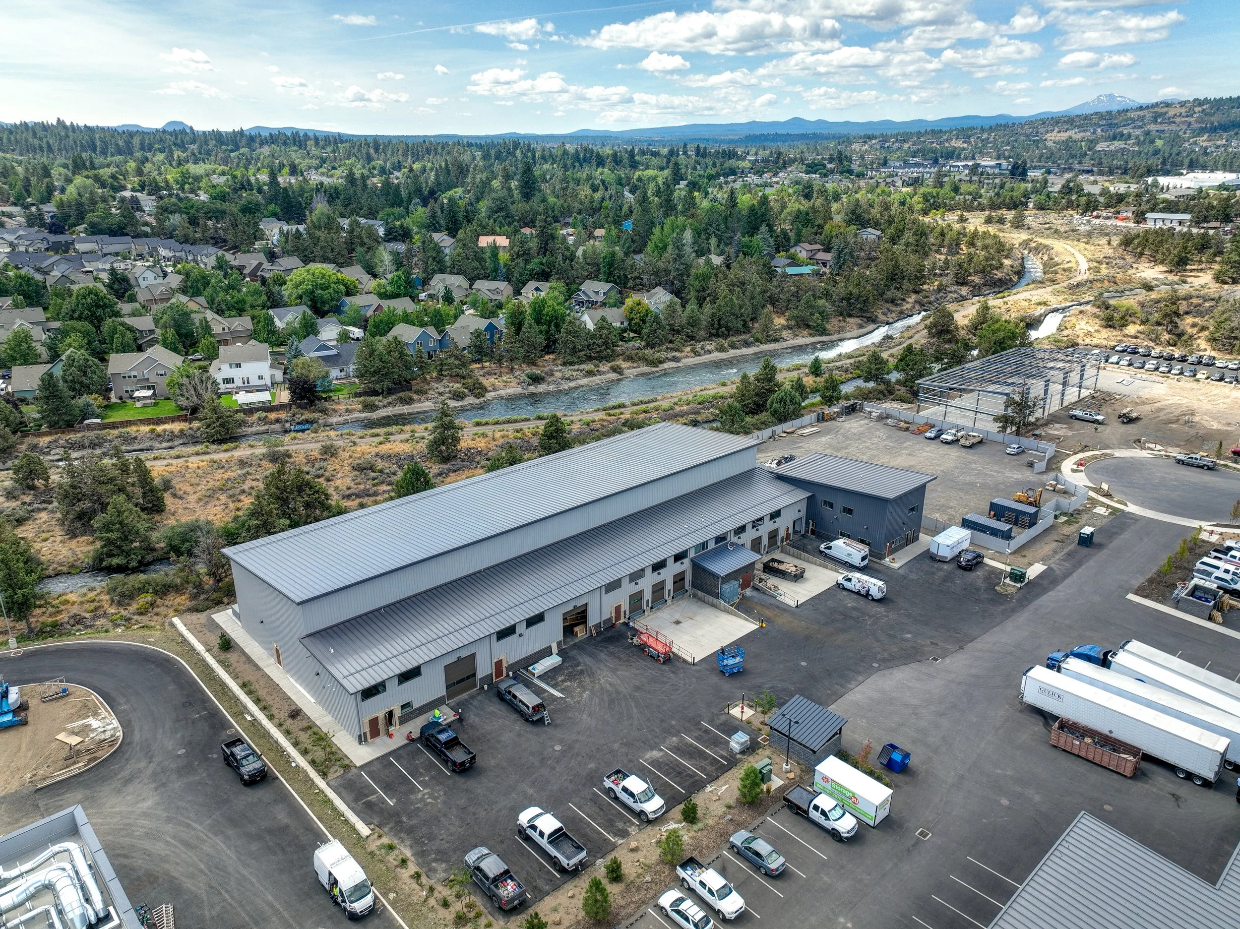 Aerial view of an industrial building with a parking lot, near a residential area and a river.