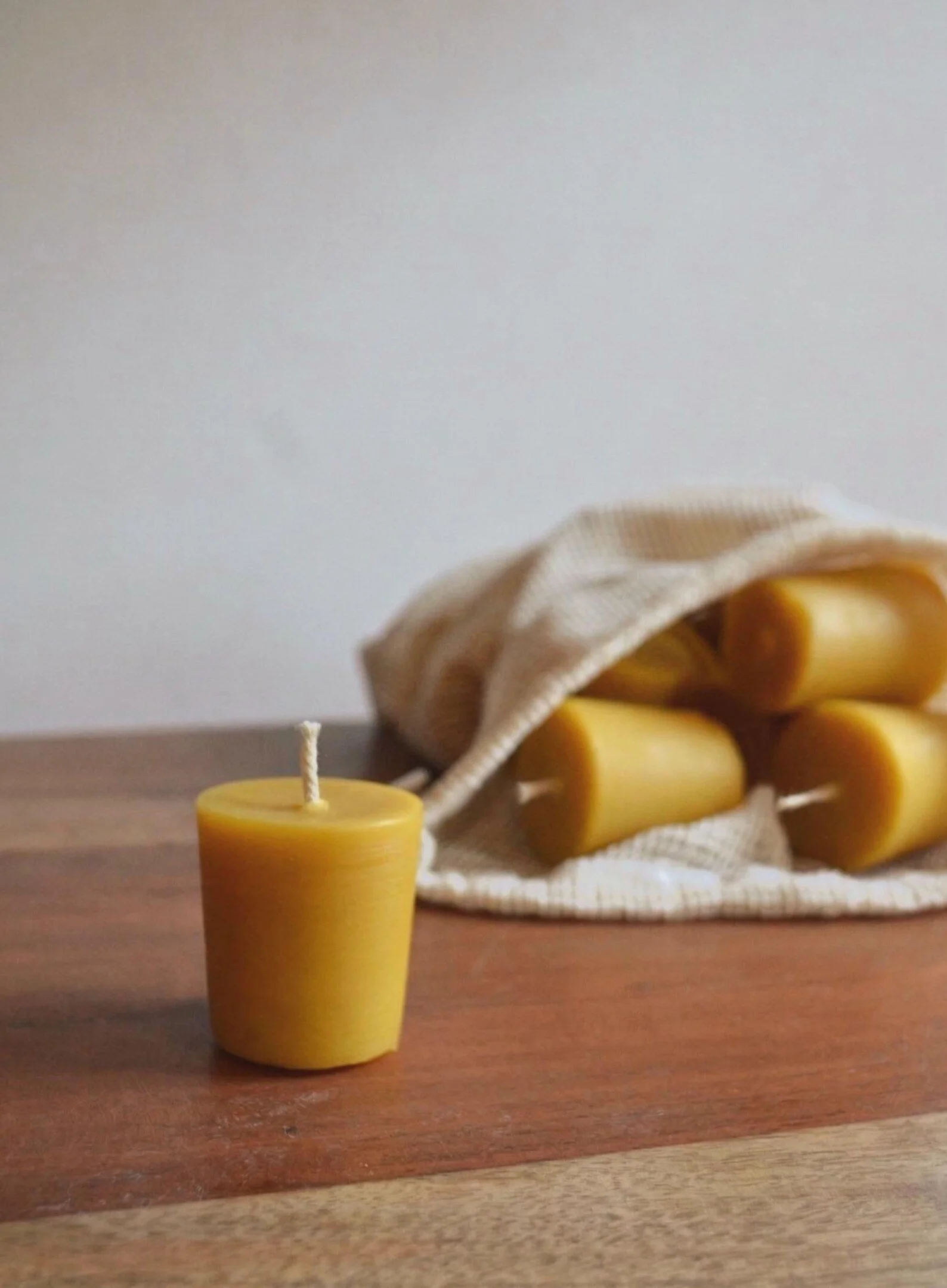 A yellow candle in the foreground on a wooden surface, with a cloth bag of similar yellow candles spilling out in the background.