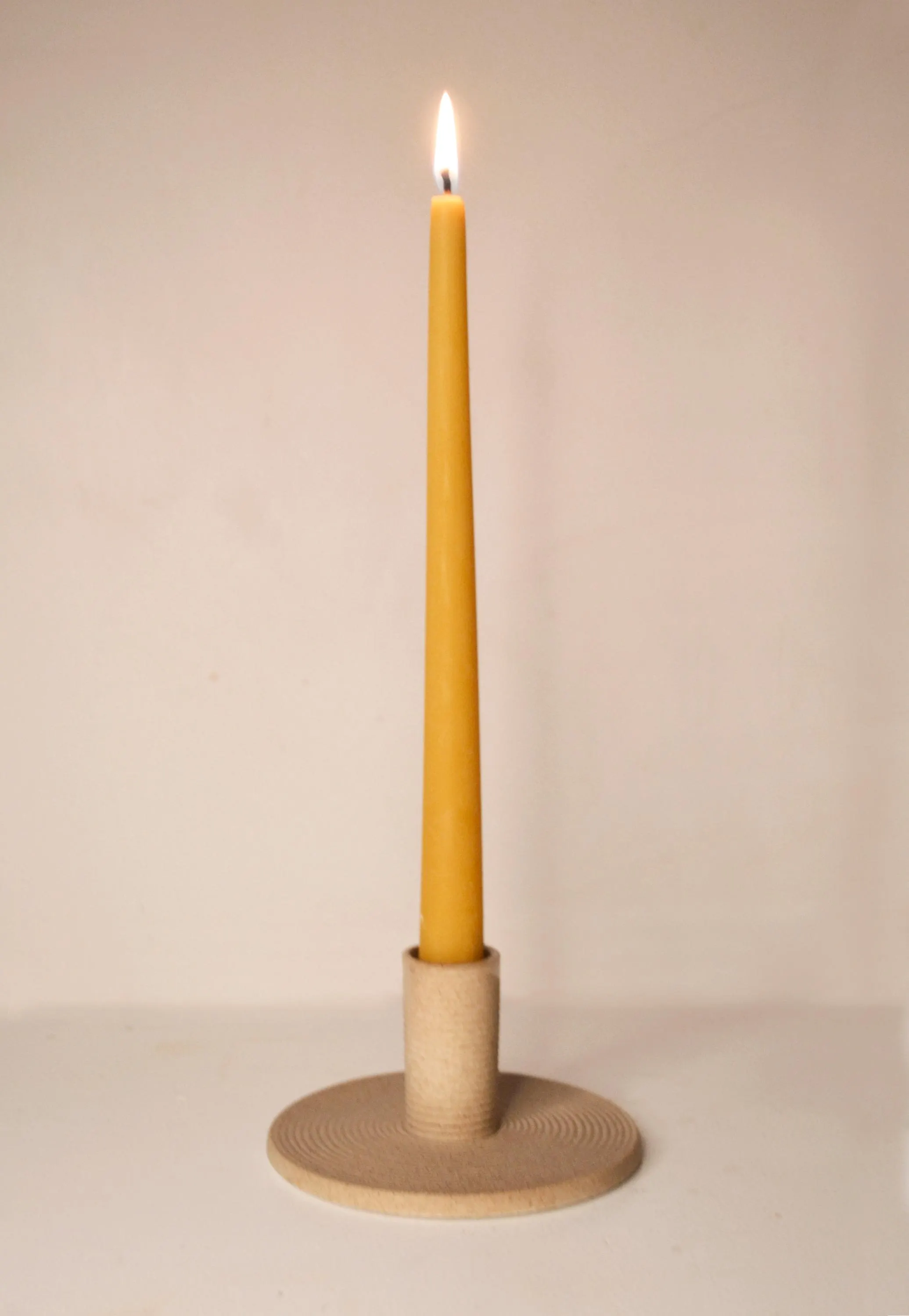 Handmade pure beeswax taper candlestick in a ceramic candle holder, lit on a neutral backdrop. Non drip clean burning tapered candle.