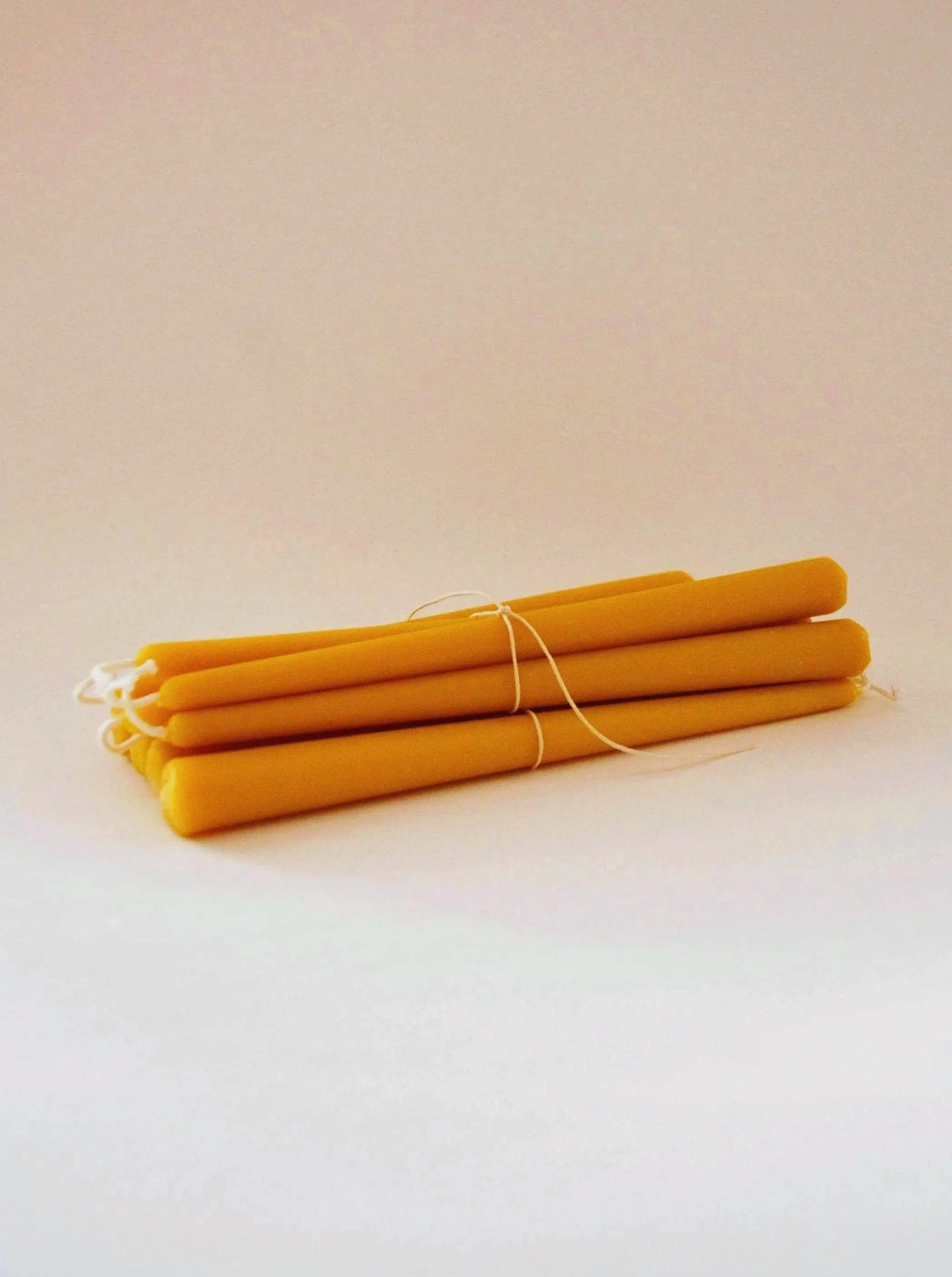 A bunch of yellow beeswax candles tied together with white string on a plain white background.