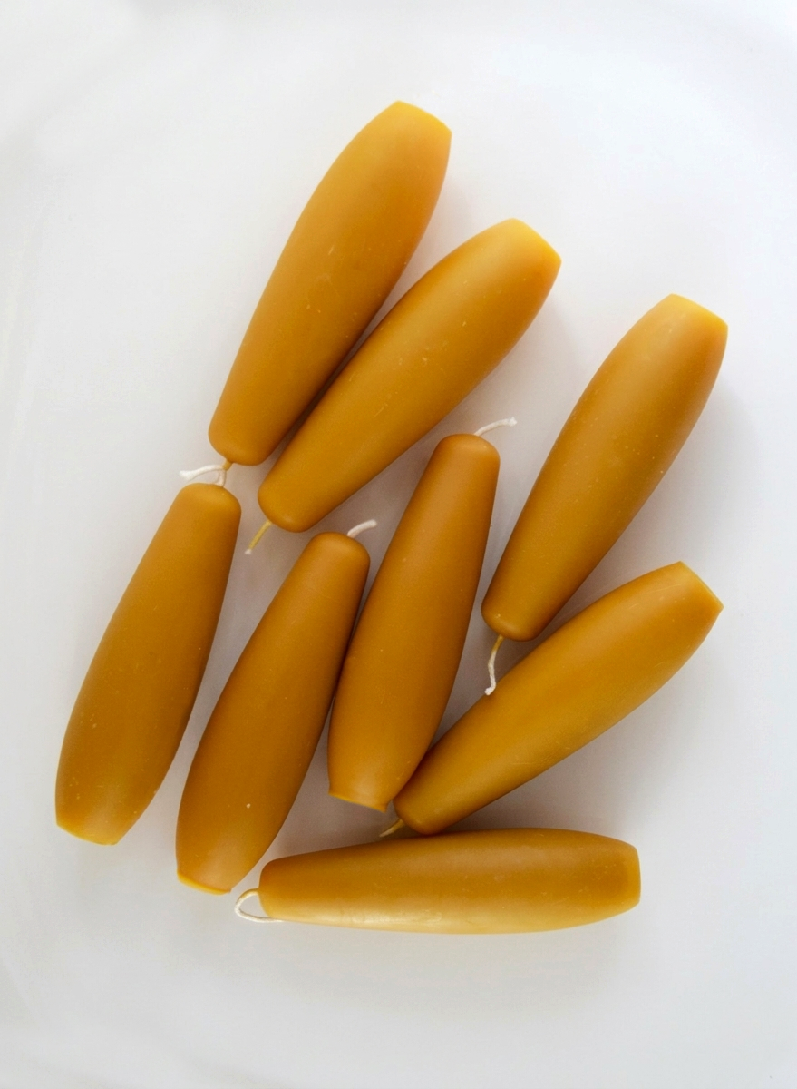Tapered stubby beeswax candles, handmade for long burning clean unscented candlelight. Eight spindle candles grouped together in natural lighting.