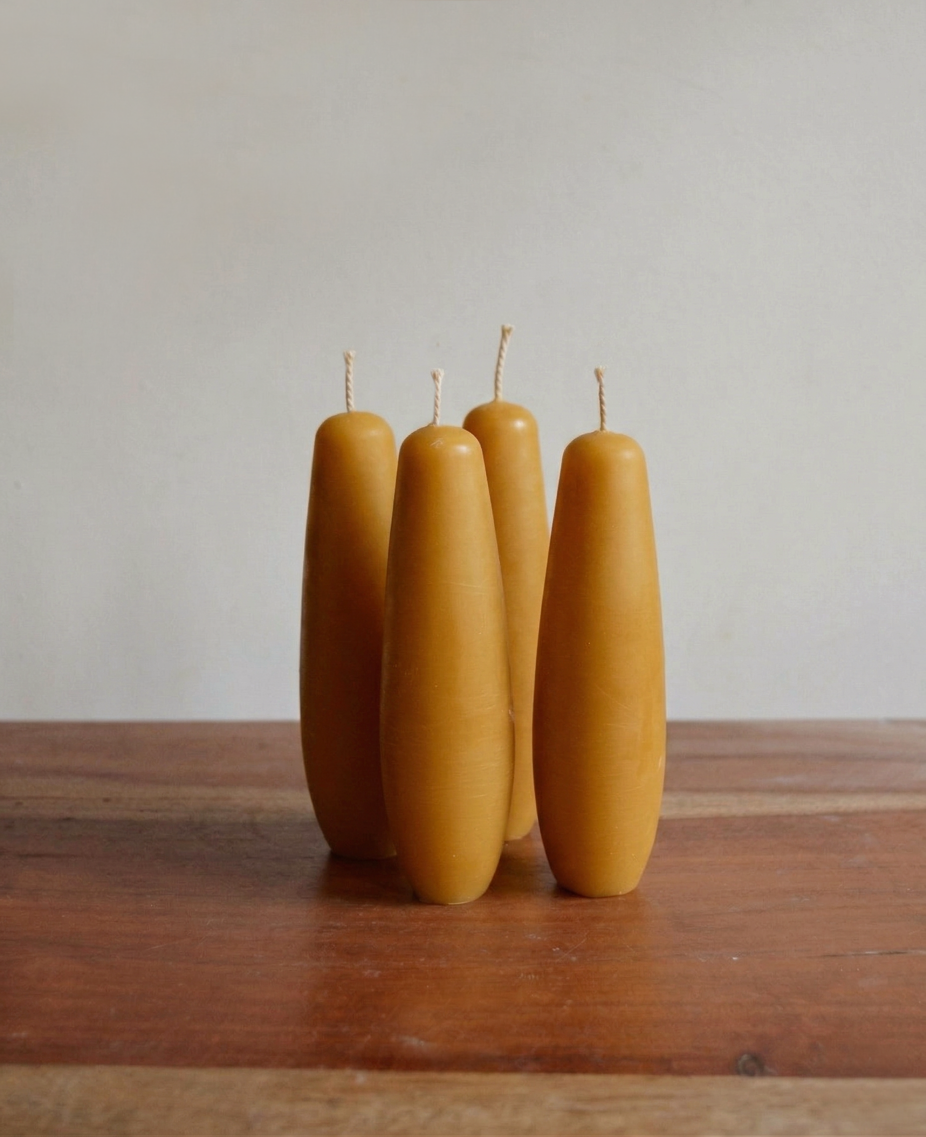 Tapered stubby beeswax candles, handmade for long burning clean unscented candlelight. Four spindle candles grouped together in natural lighting.