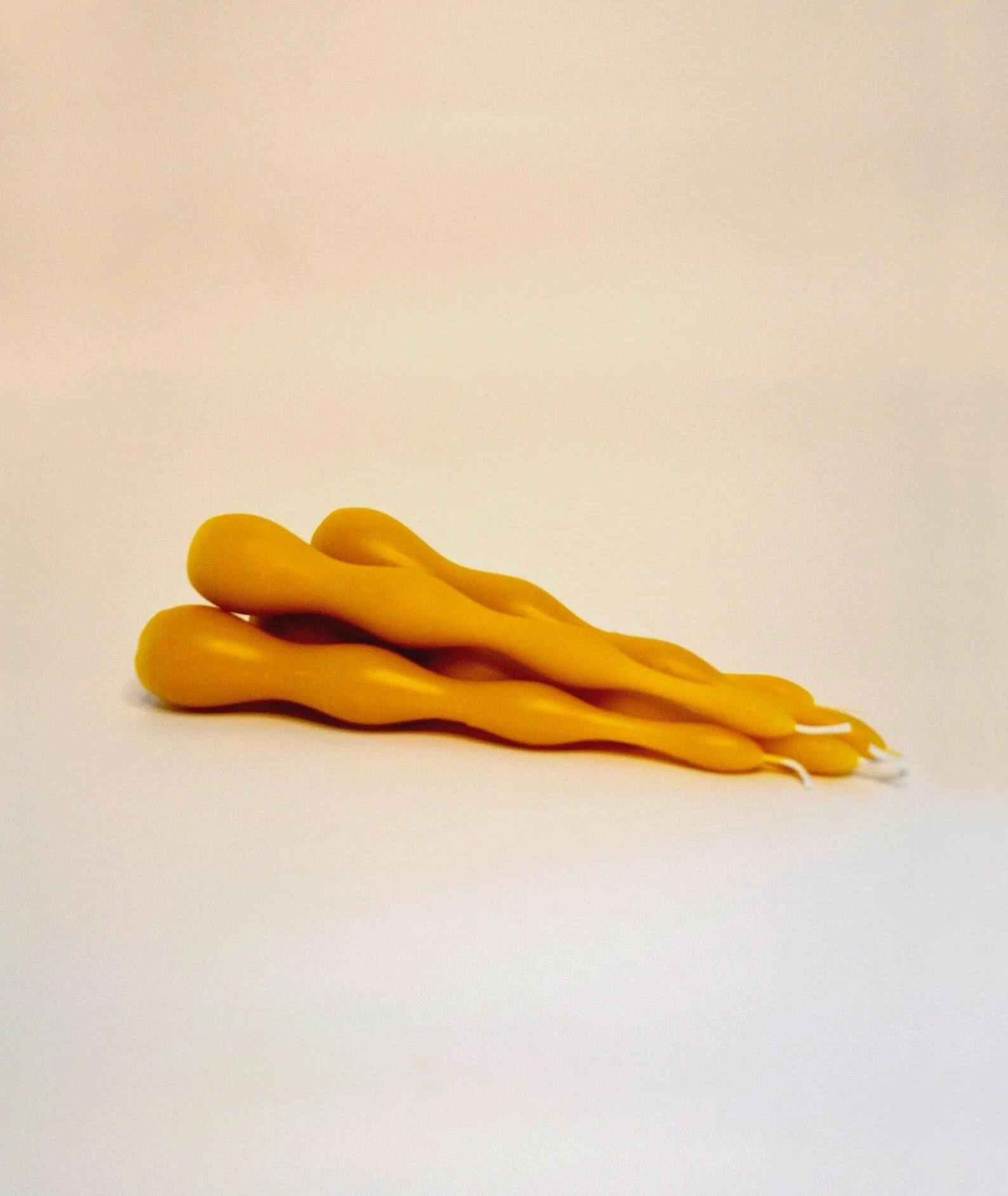 Four yellow twisted candles stacked on top of each other against a plain background.