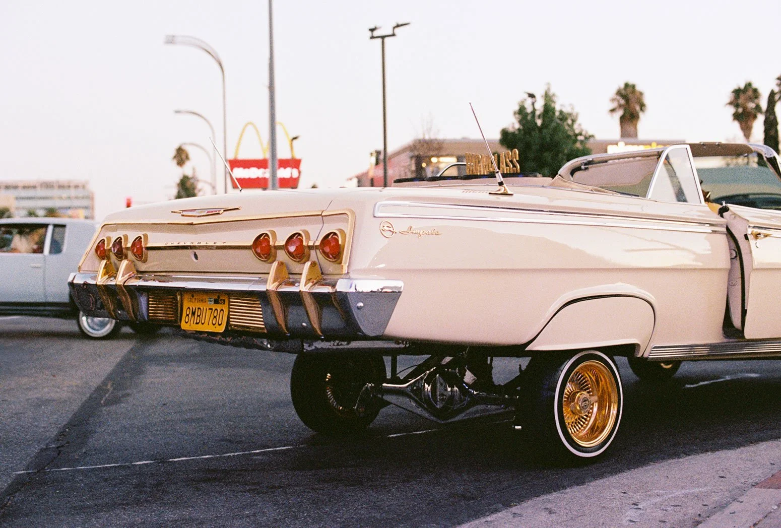A vintage white and gold Chevrolet convertible car with a California license plate parked on a street during sunset.