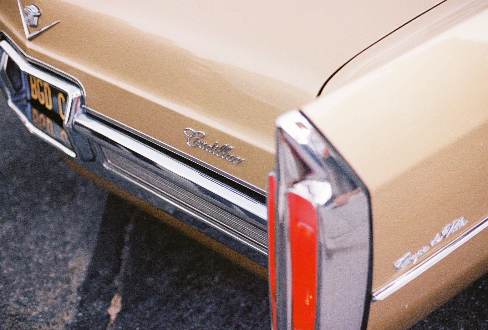 Close-up of the back of a vintage gold Cadillac car, showing the Cadillac badge and part of the tail light.