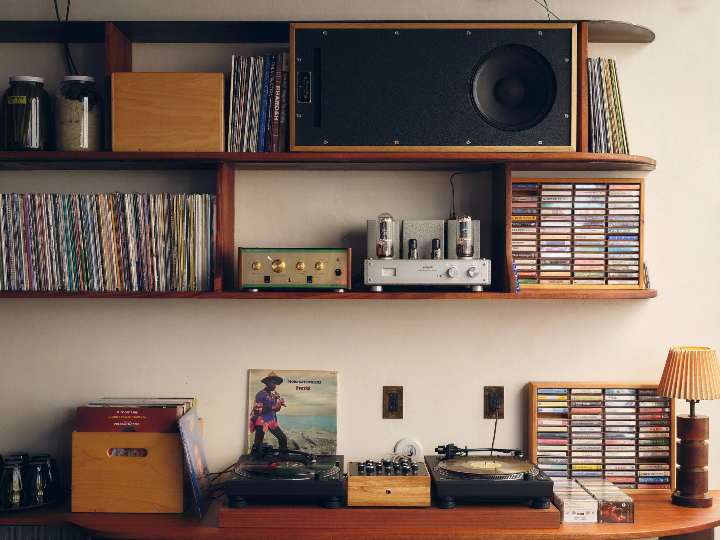 A wooden shelving unit holding vinyl records, books, a vintage stereo system with turntables and speakers, and decorative items including jars and a lamp.