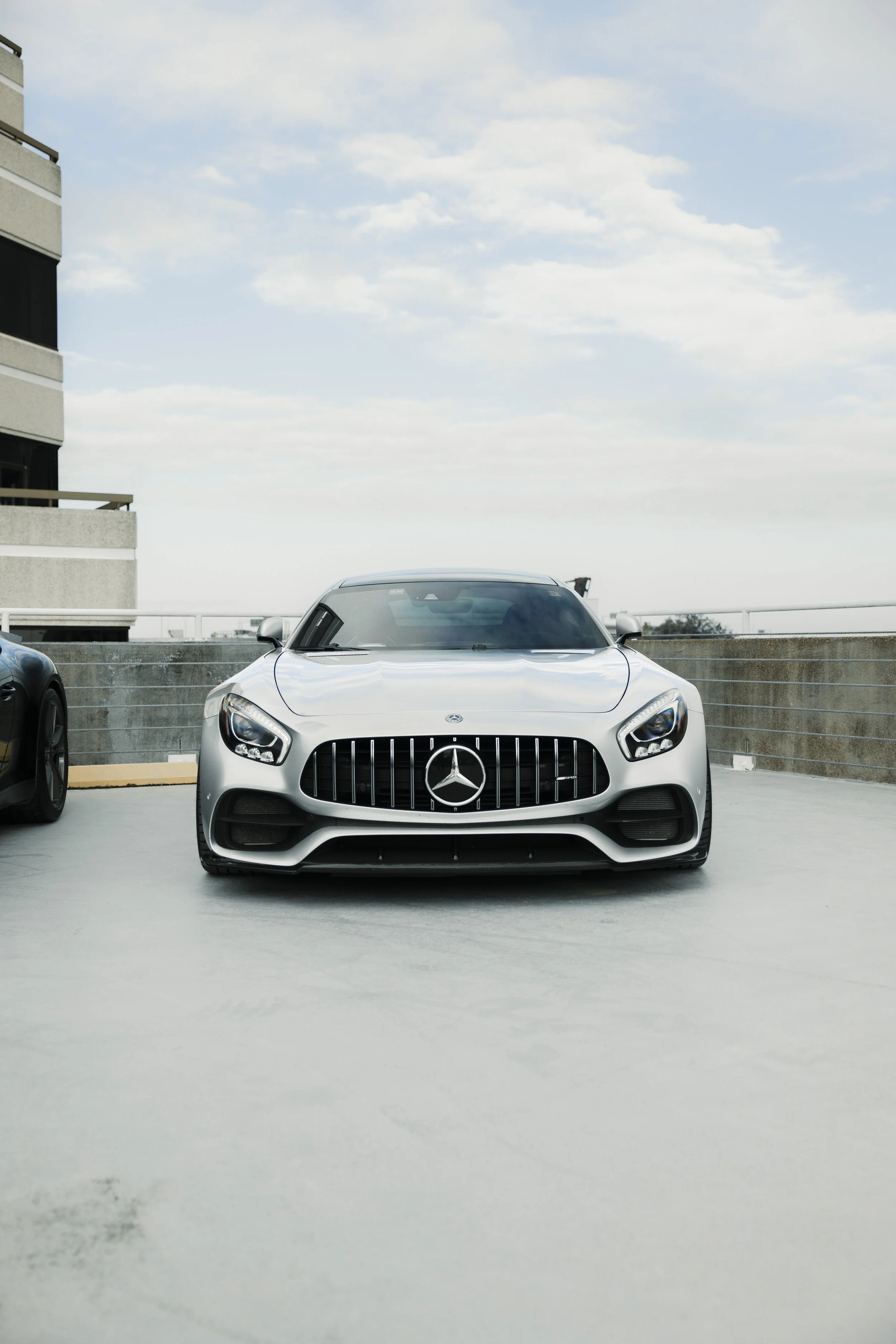 Silver Mercedes-Benz sports car parked in an outdoor parking lot under a cloudy sky.