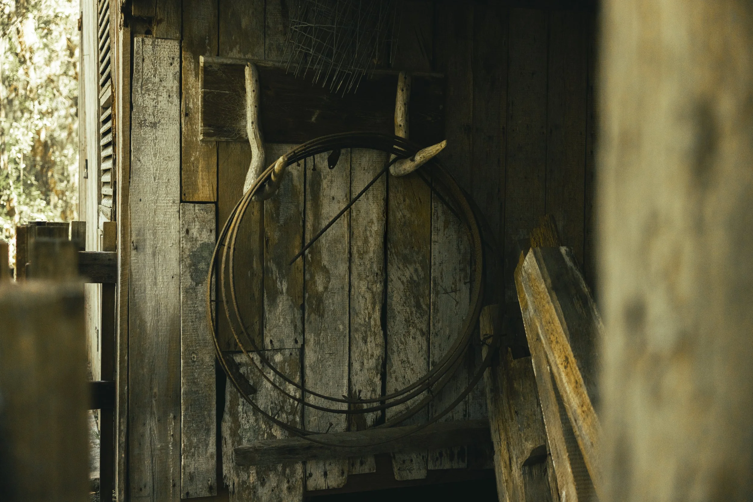A rustic wooden wall decorated with a vintage bicycle wheel, a pair of old antlers, a wooden shelf, and various farm tools.