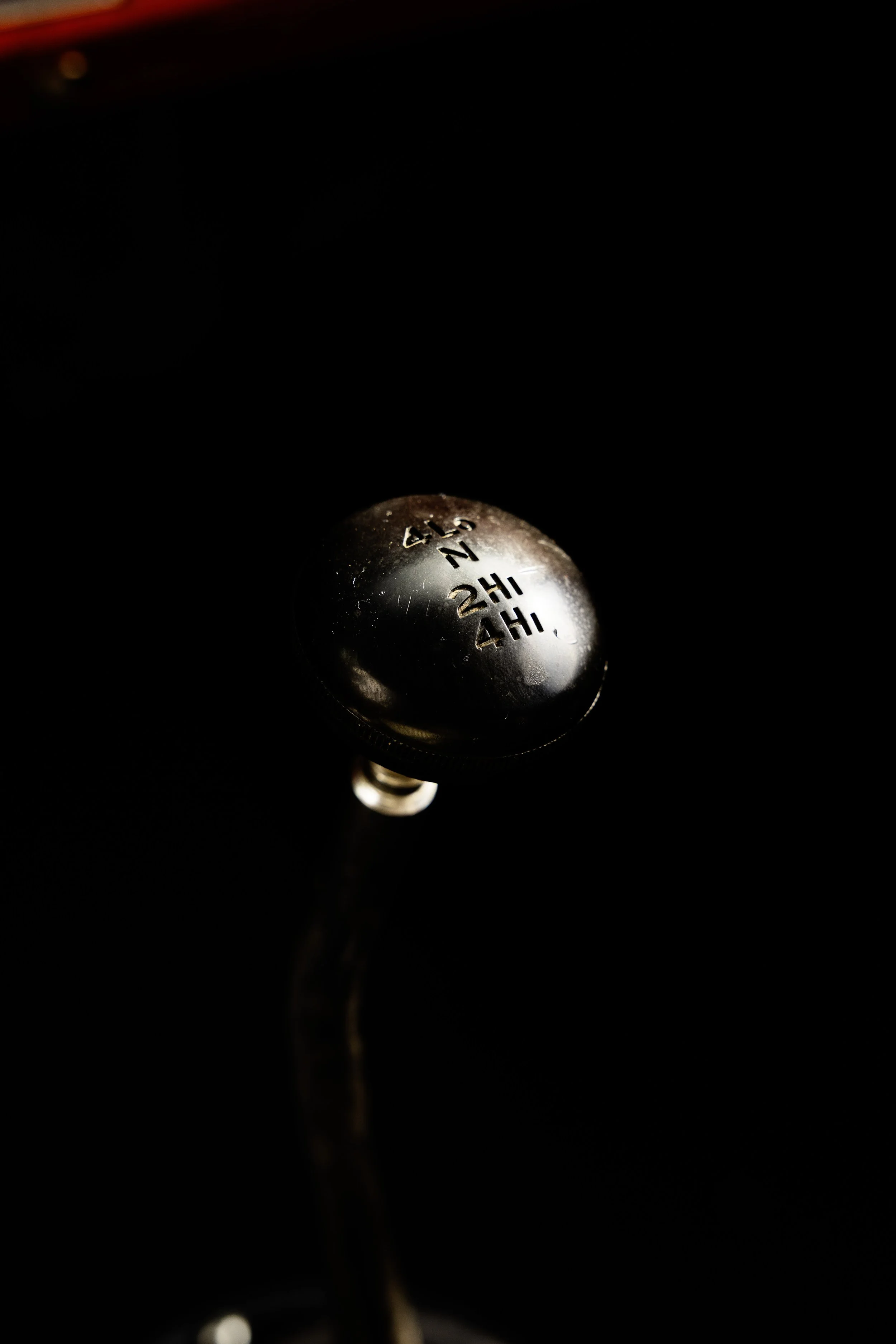 Close-up of a manual gear shift knob with gear positions labeled, set against a dark background.