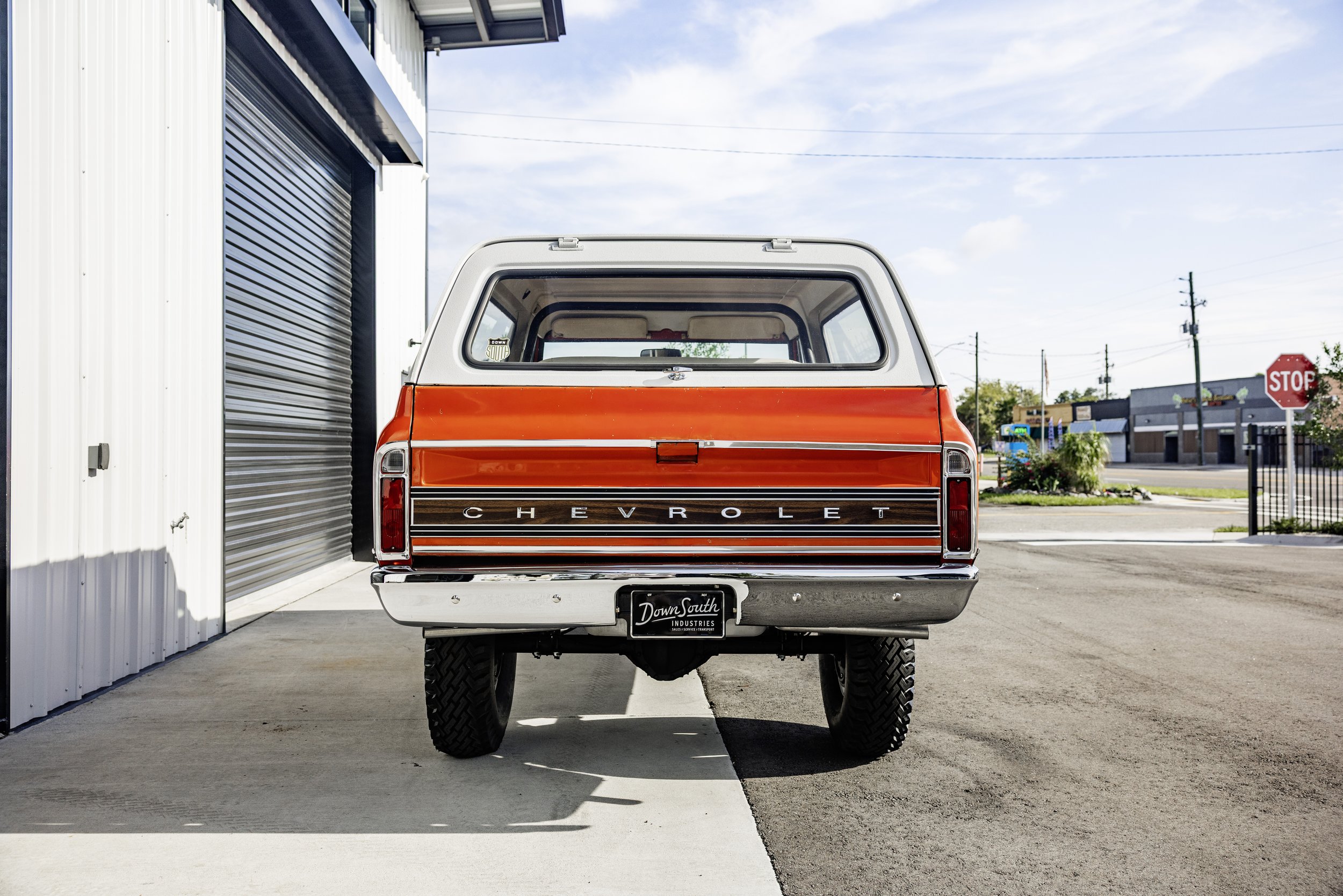 Rear view of a vintage red and white Chevrolet pickup truck parked outside a metal building with a closed roll-up door, in a small town or commercial area.