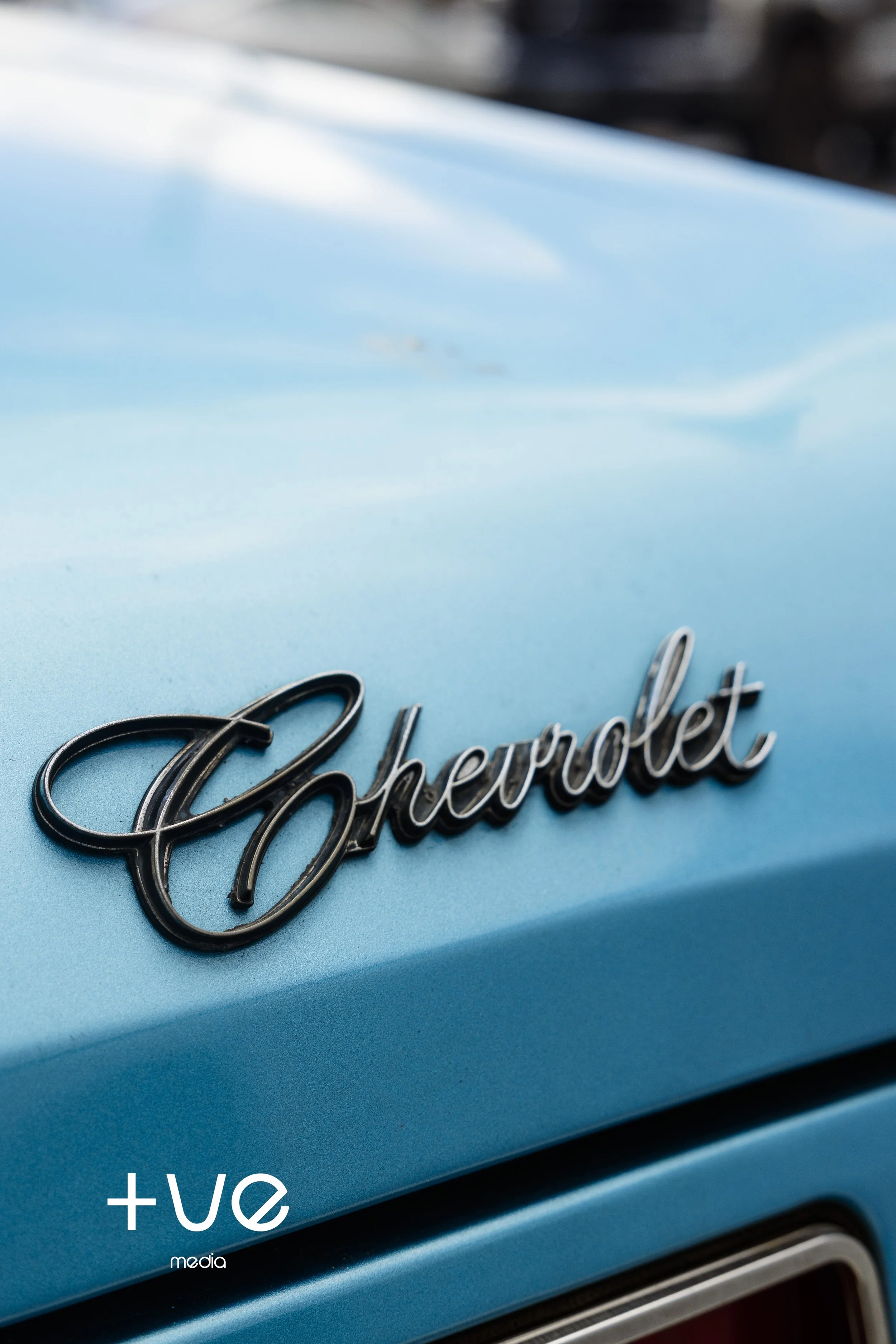 Close-up of a vintage Chevrolet emblem on a light blue car.