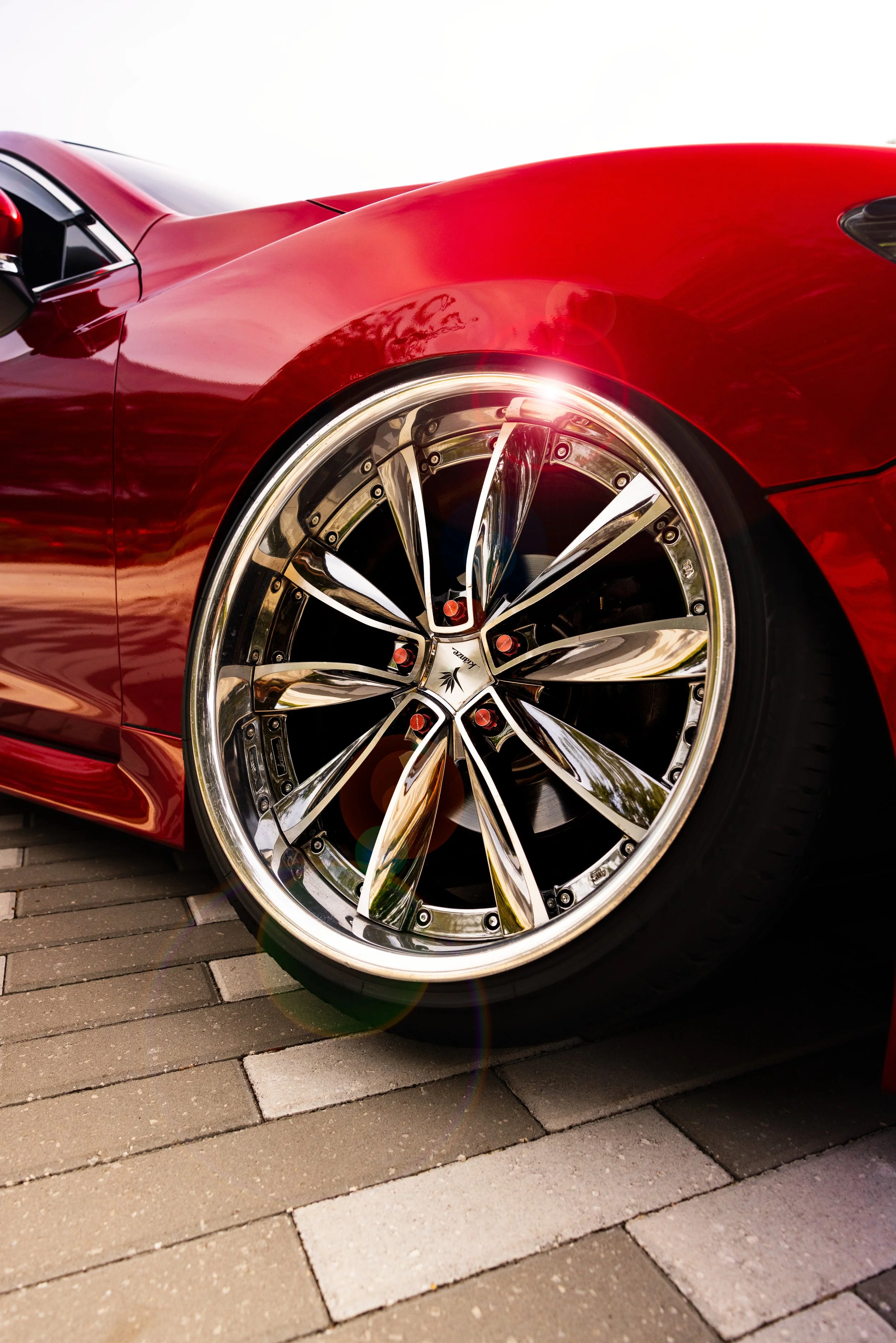Close-up of a red sports car with shiny, alloy wheels parked on a paved surface.