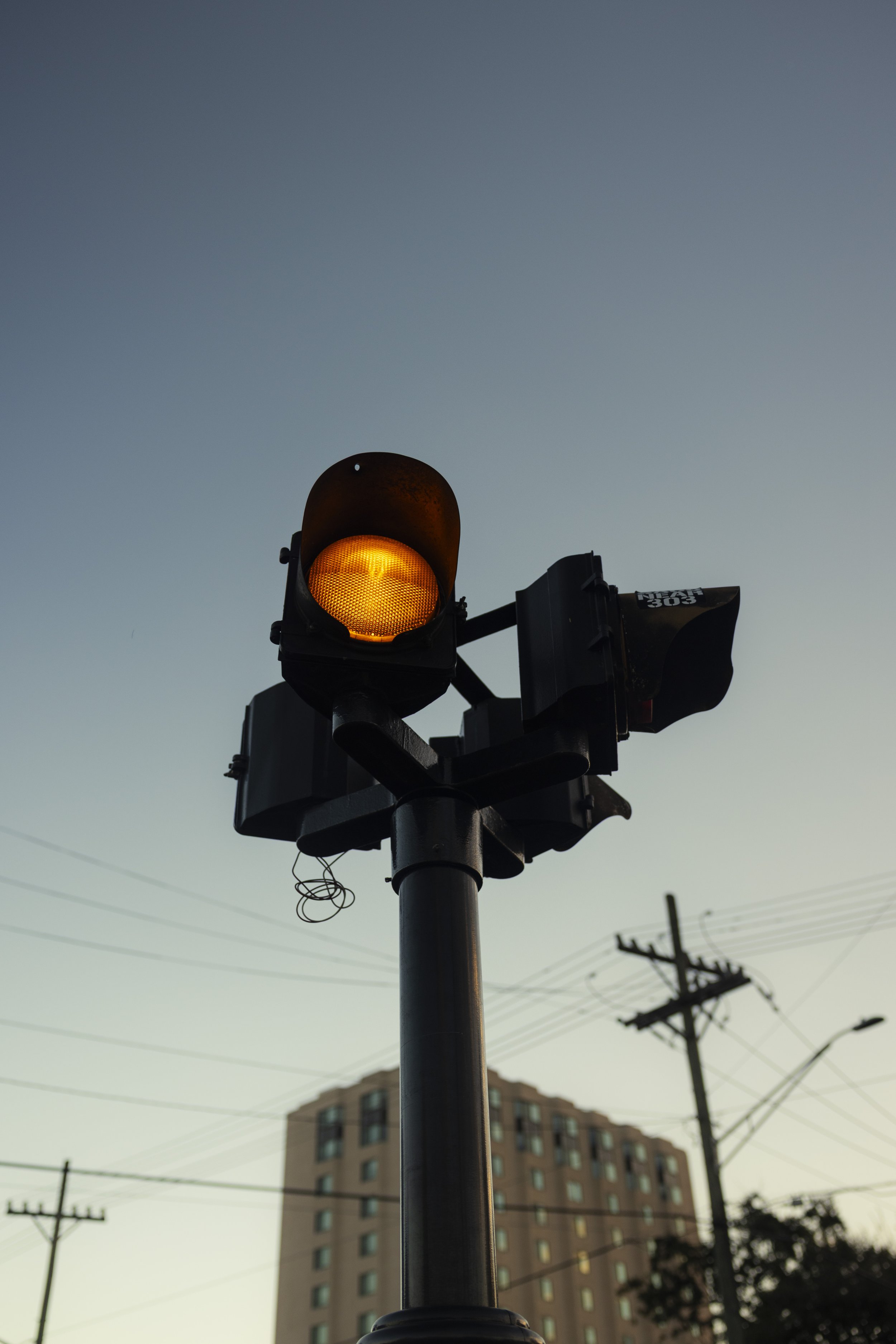 Traffic light displaying a yellow or amber signal, silhouette view against a clear evening sky.