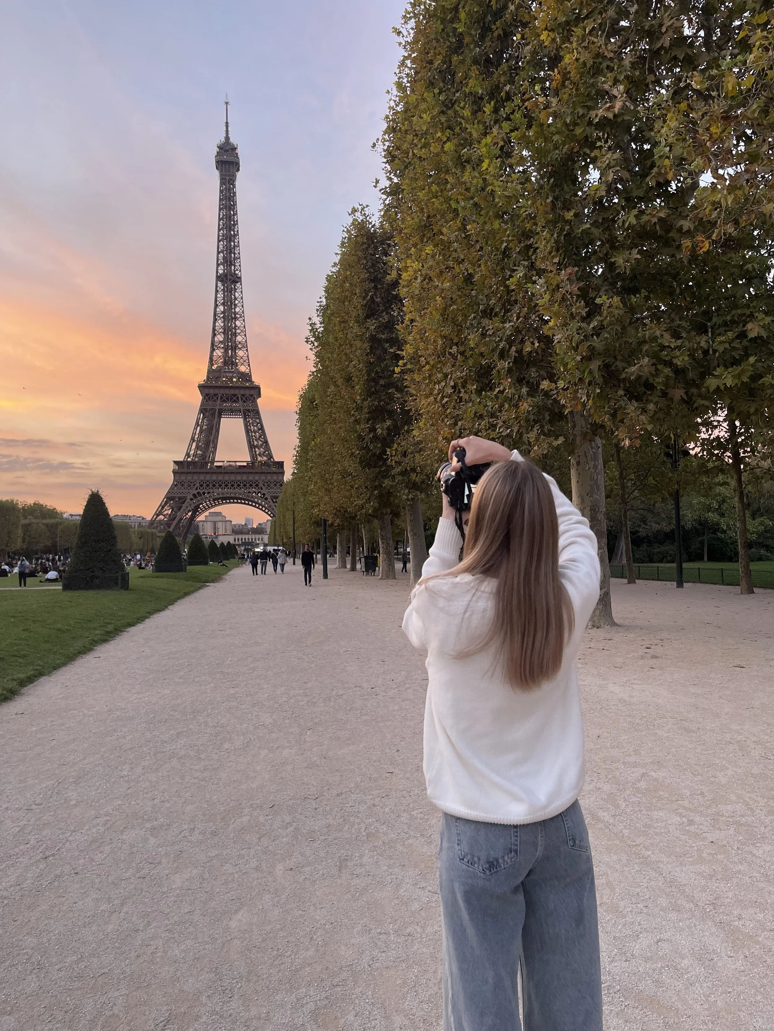 A person with long hair taking a photo of the Eiffel Tower at sunset in Paris, France.