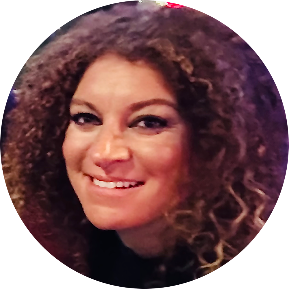 Close-up of a smiling woman with curly hair and makeup.