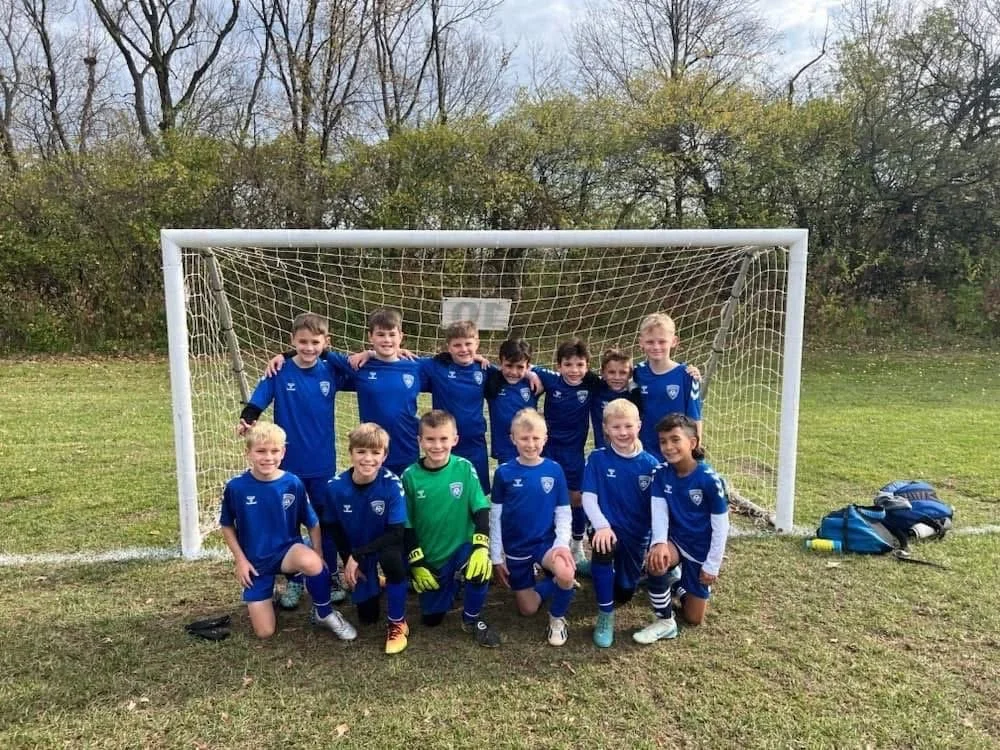 A group of young boys in blue soccer uniforms posing in front of a soccer goal on a grassy field.