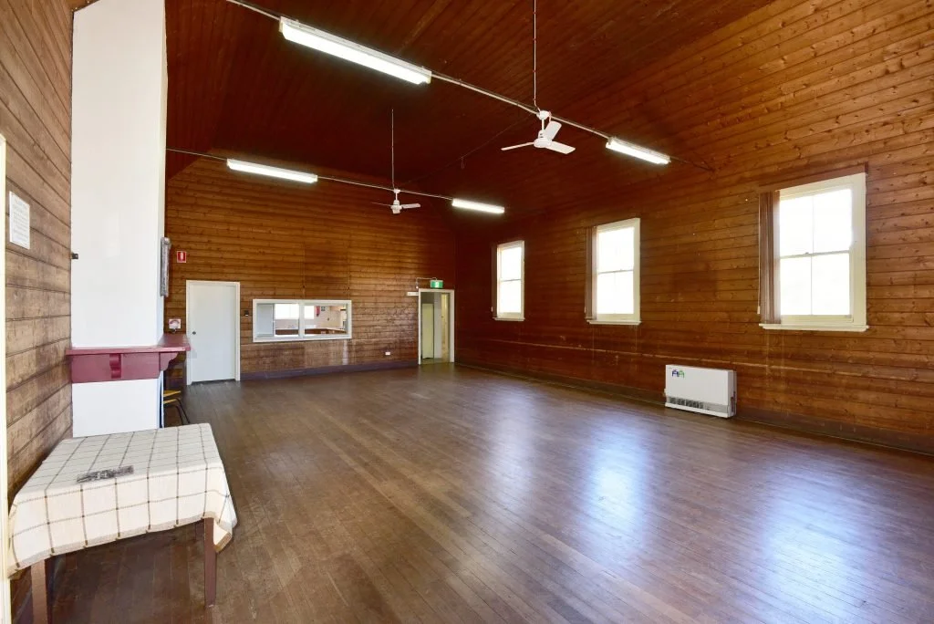 Empty wooden hall with high ceiling, windows, ceiling fans, and a small table with a checkered cloth.