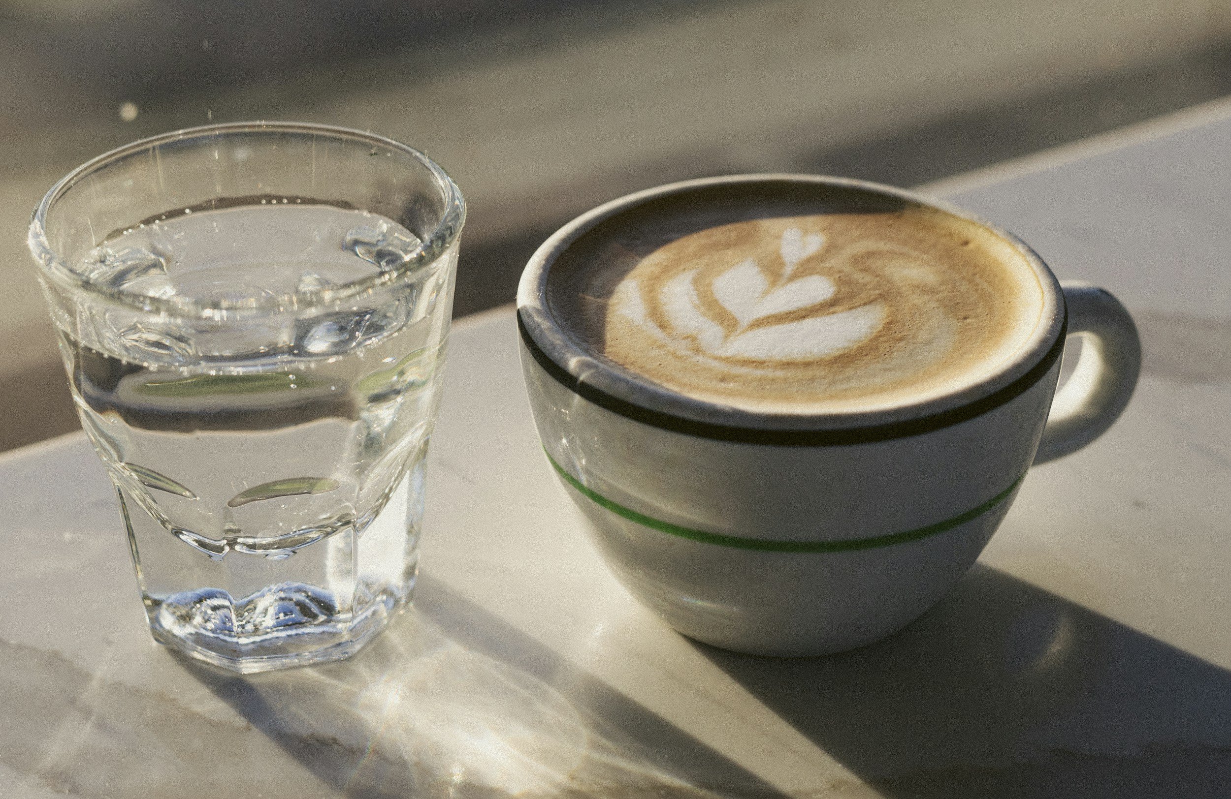 Glass of water next to a latte on a kitchen counter, representing natural ways to boost energy without relying on caffeine.