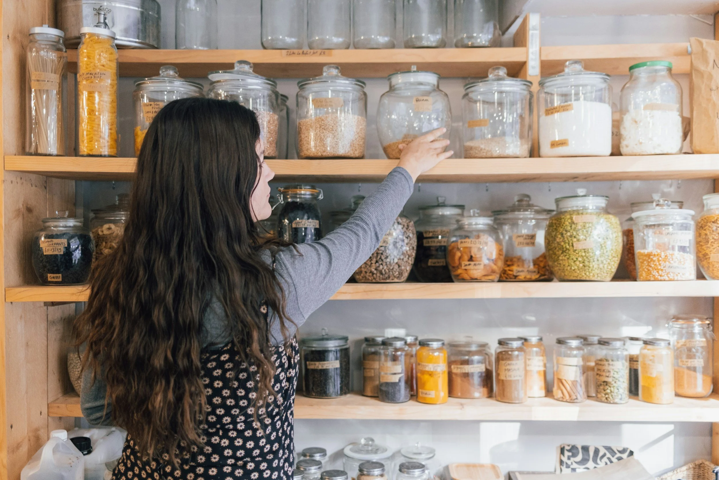 Woman reaching for whole food ingredients in her pantry, showing how planning ahead can help stop stress eating as a mom