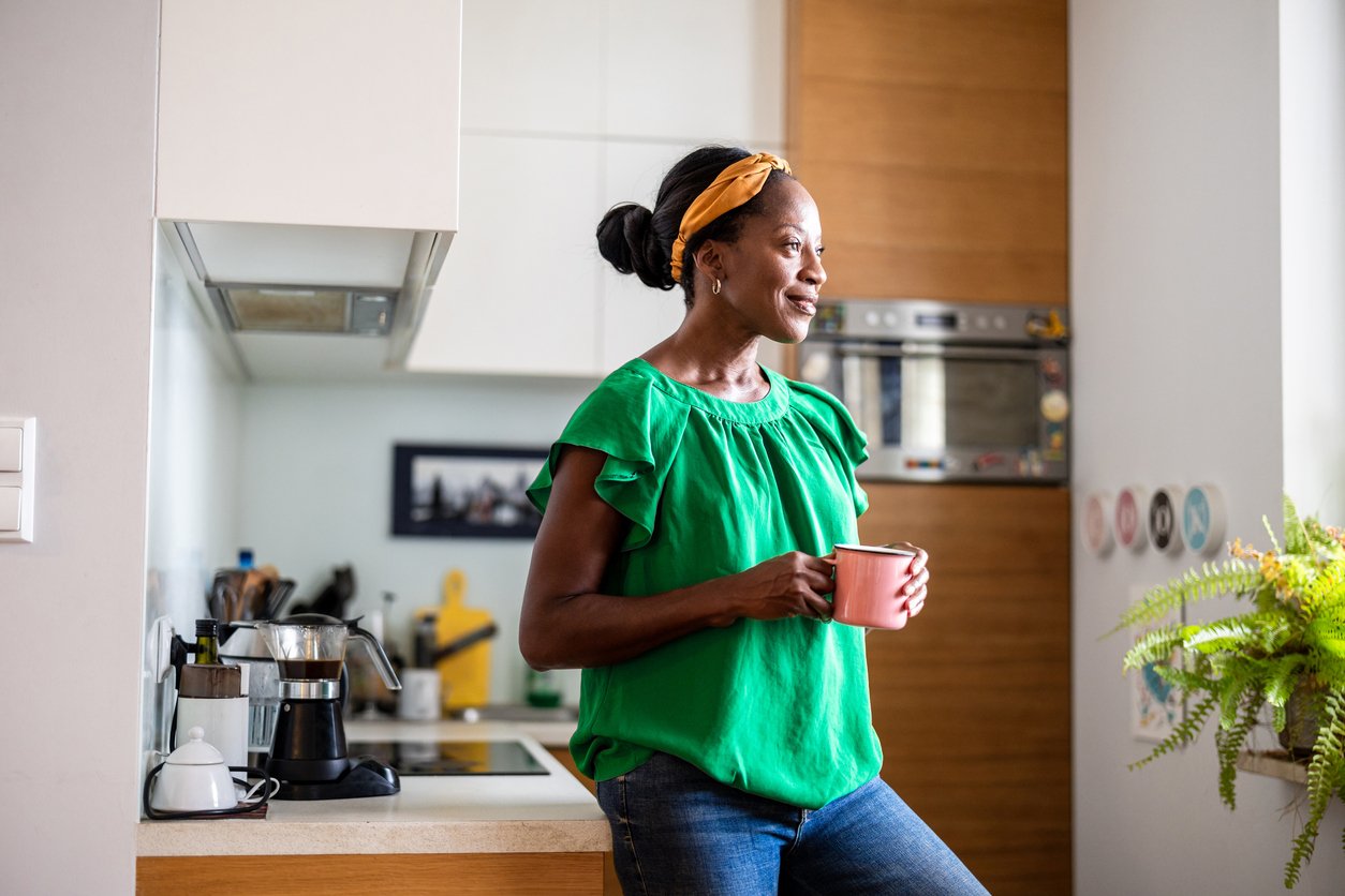 Woman in midlife standing in kitchen at night, representing food cravings during menopause caused by hormonal changes.