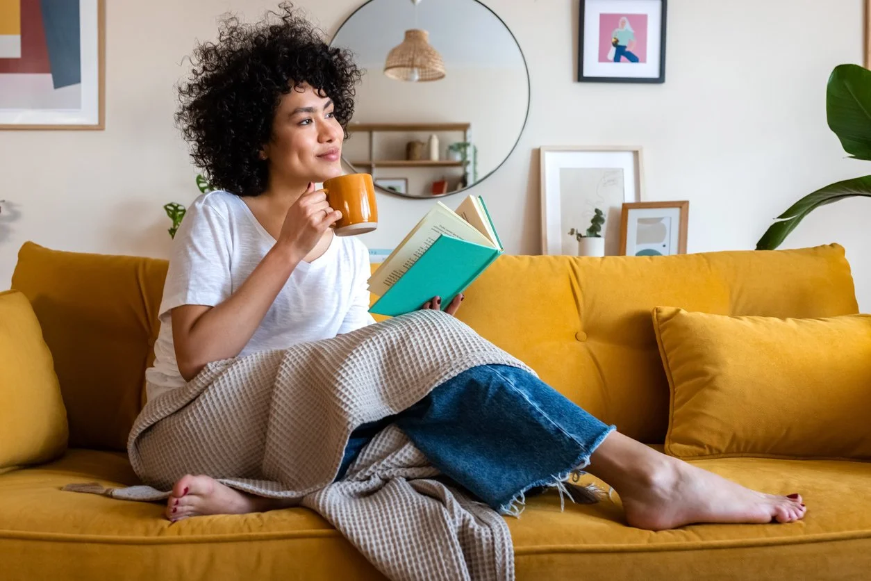 Woman pausing with a cup of tea on the couch, demonstrating the pause technique to interrupt stress eating urges.