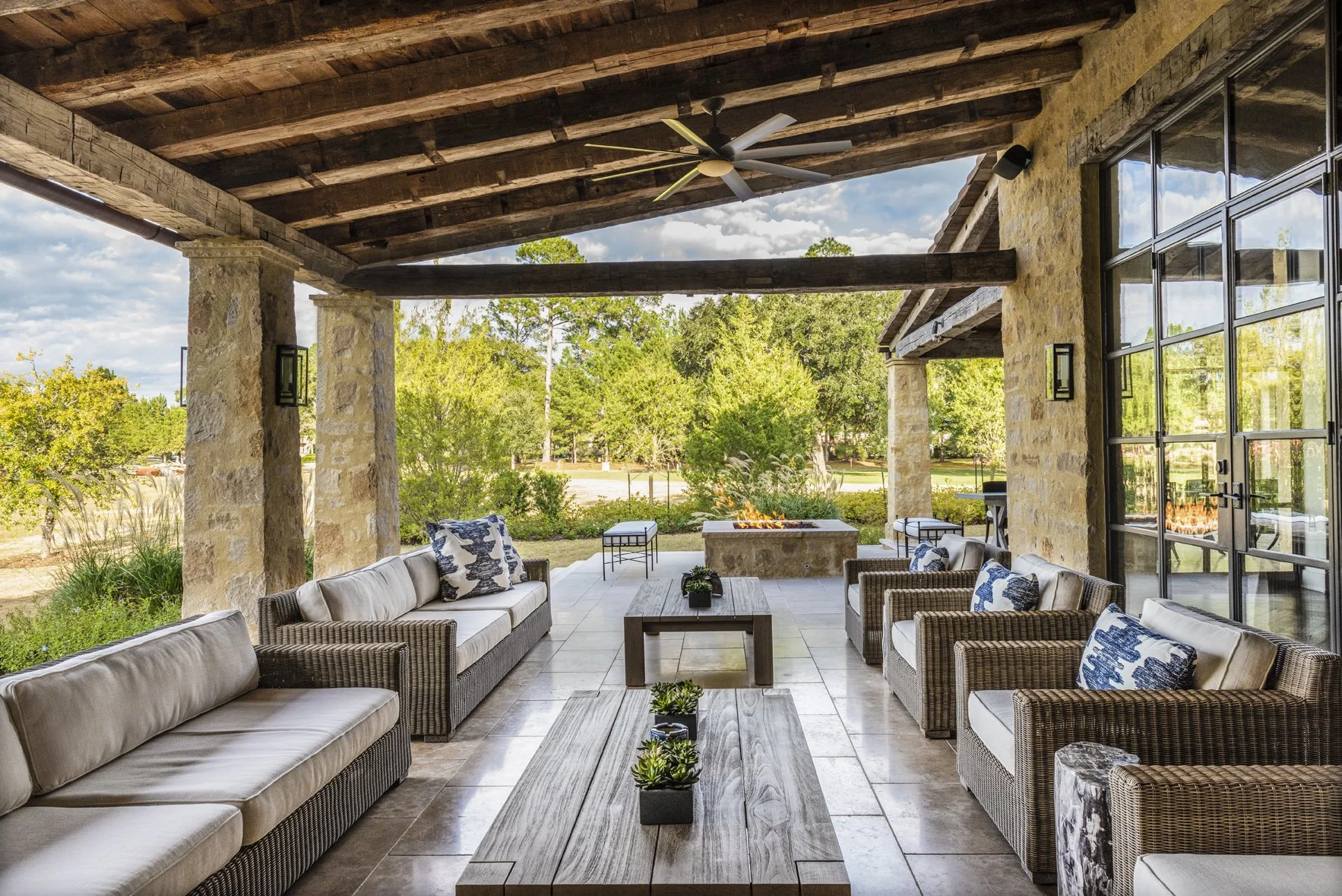 Modern ranch covered patio with reclaimed wood beams, woven seating, stone columns and a garden fire pit.