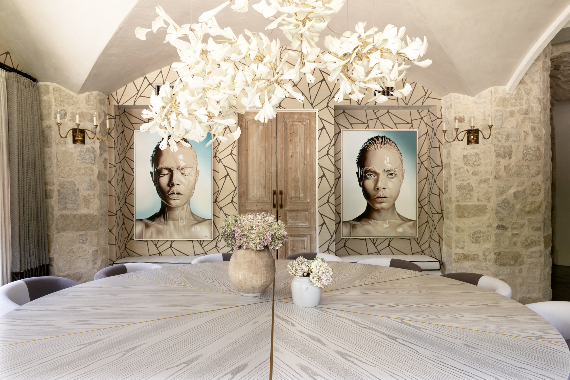 French country home in Houston dining room with a large round wood table, stone walls and a white sculptural chandelier.