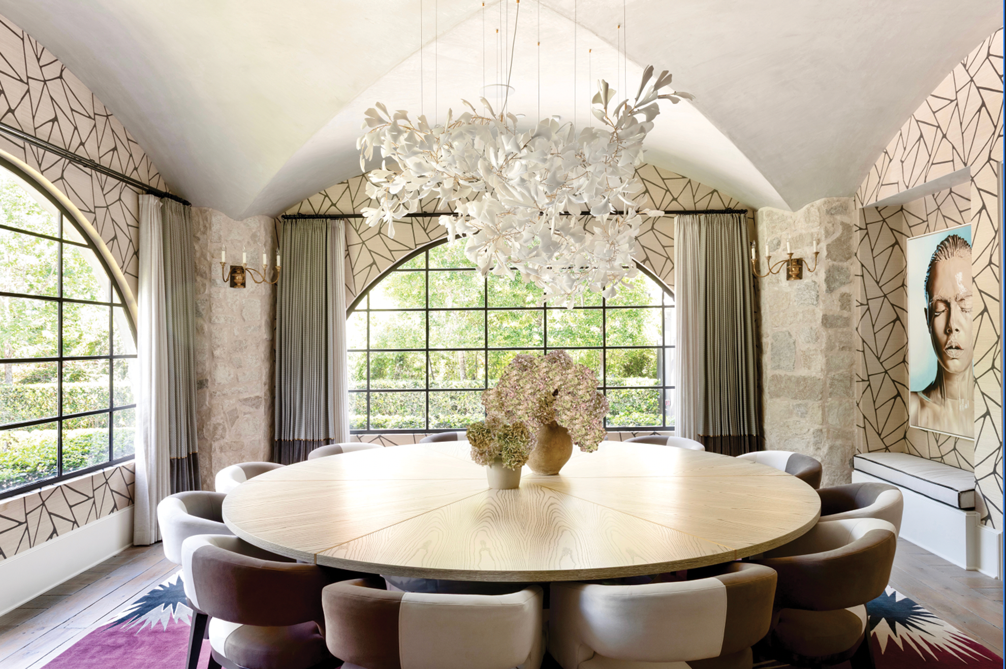French country home in Houston dining room with a round wood table, hydrangeas, arched windows and sculptural chandelier.