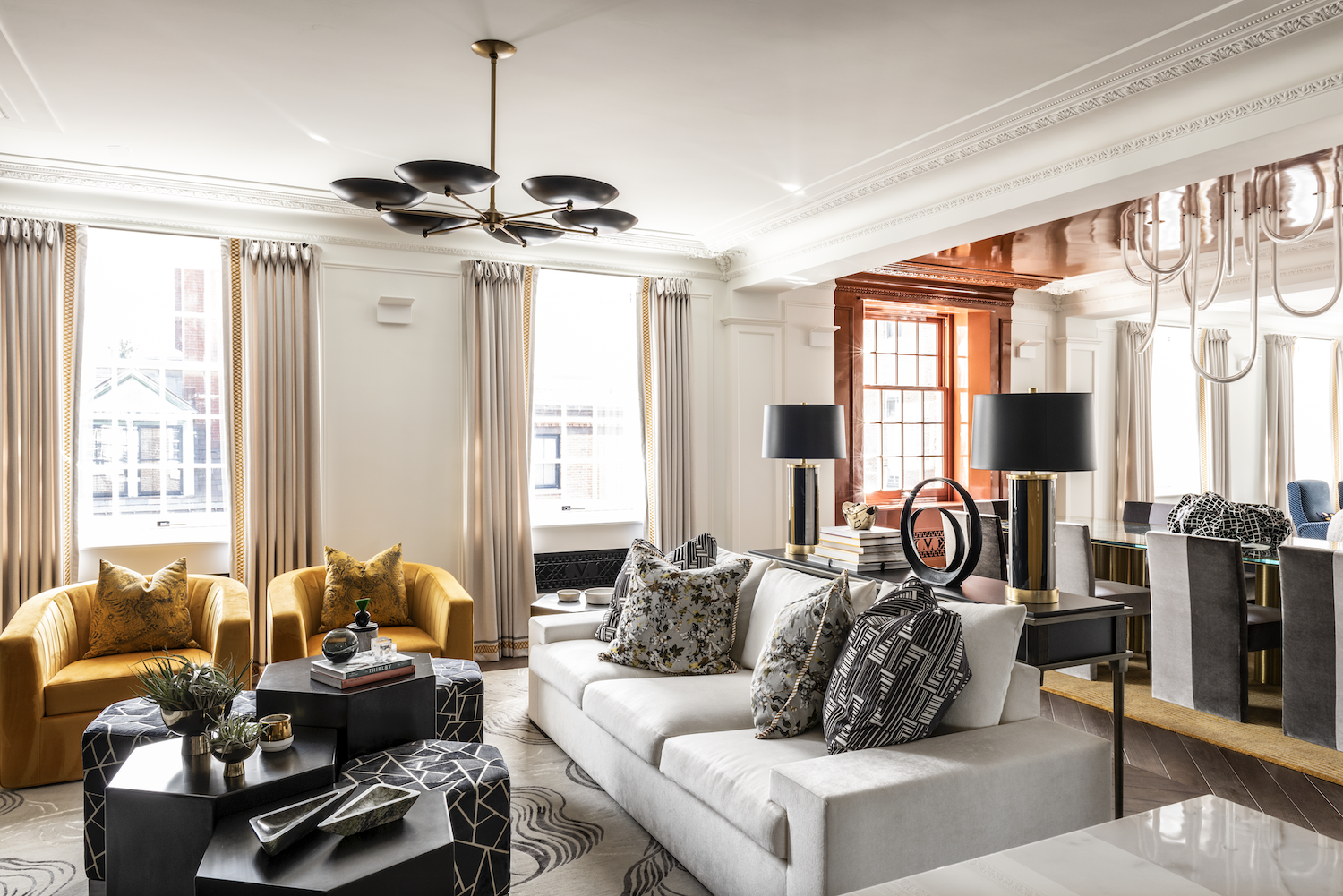 New York living and dining interior with gold lounge chairs, layered textiles, custom drapery and a copper-toned ceiling.