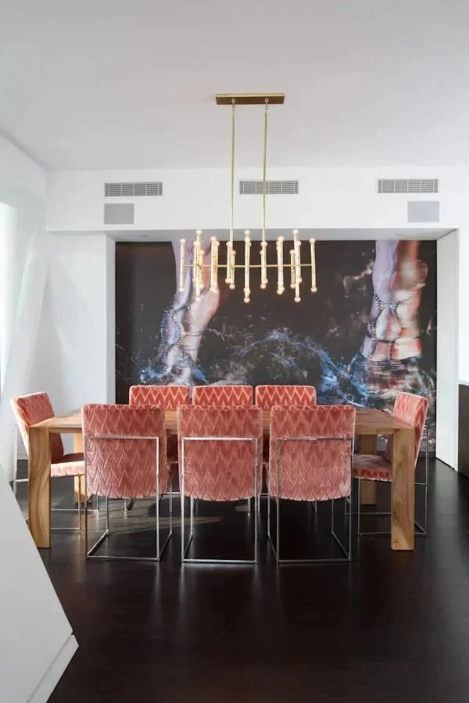 Highline apartment dining room with coral upholstered chairs, a gold chandelier and dramatic photographic artwork.