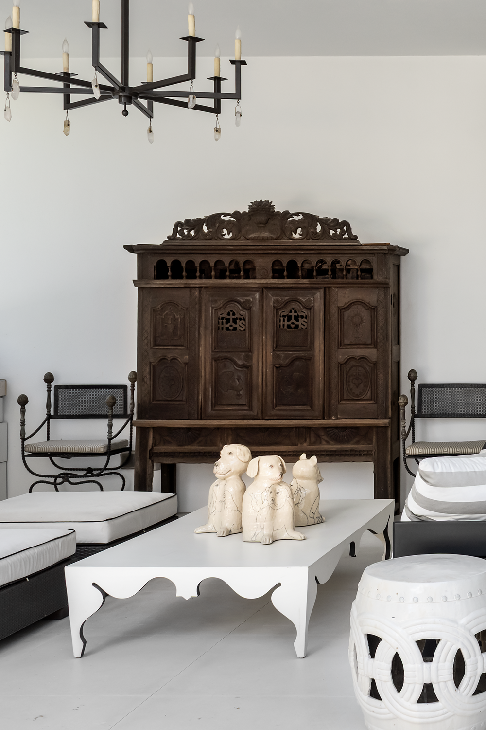 Modern luxury home in Houston outdoor lounge with an antique carved cabinet, black chandelier and monochrome seating.