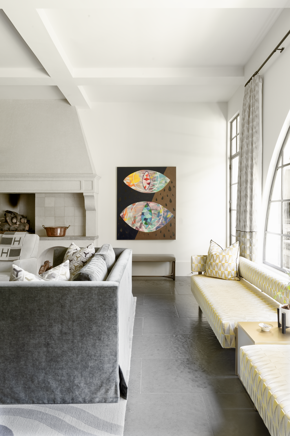 French country home in Houston sitting area with a patterned window seat, arched steel window and colourful eye artwork.