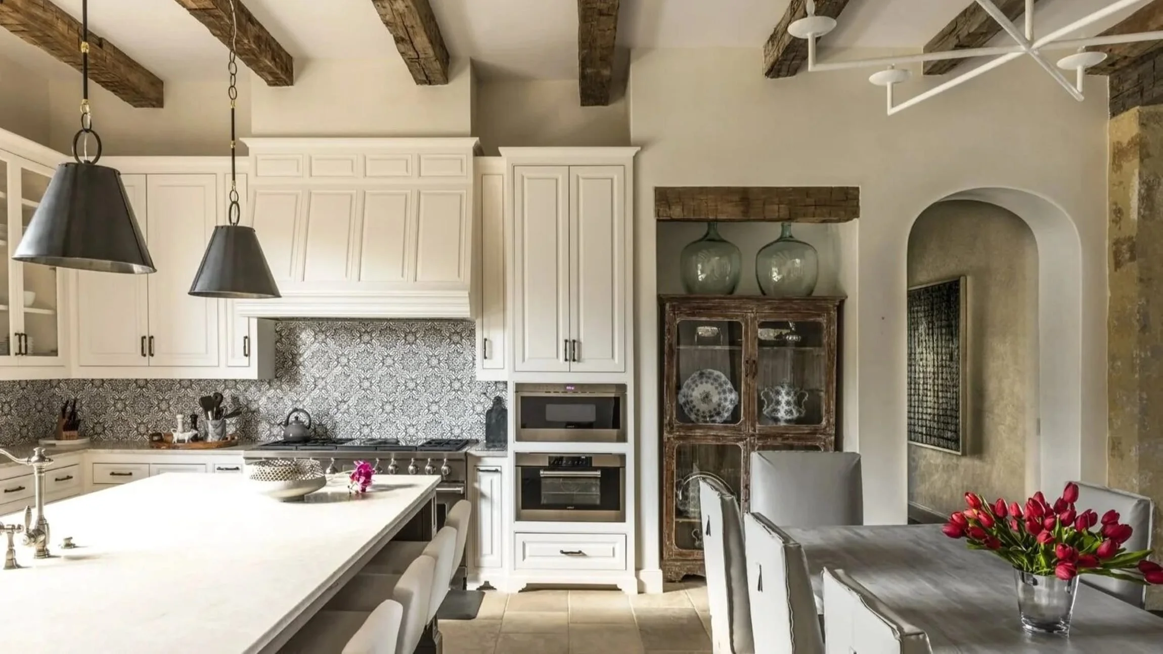 Houston Oaks residence kitchen with white cabinetry, patterned backsplash, rustic beams and an adjoining dining area.