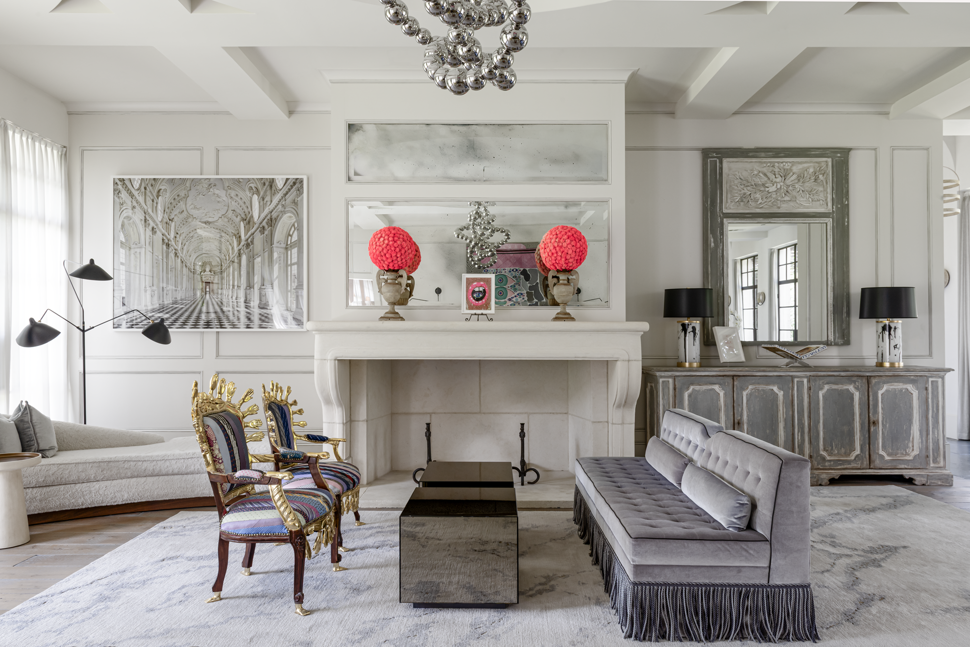 French country home in Houston living room with a limestone fireplace, fringed sofa, sculptural chairs and bold artwork.